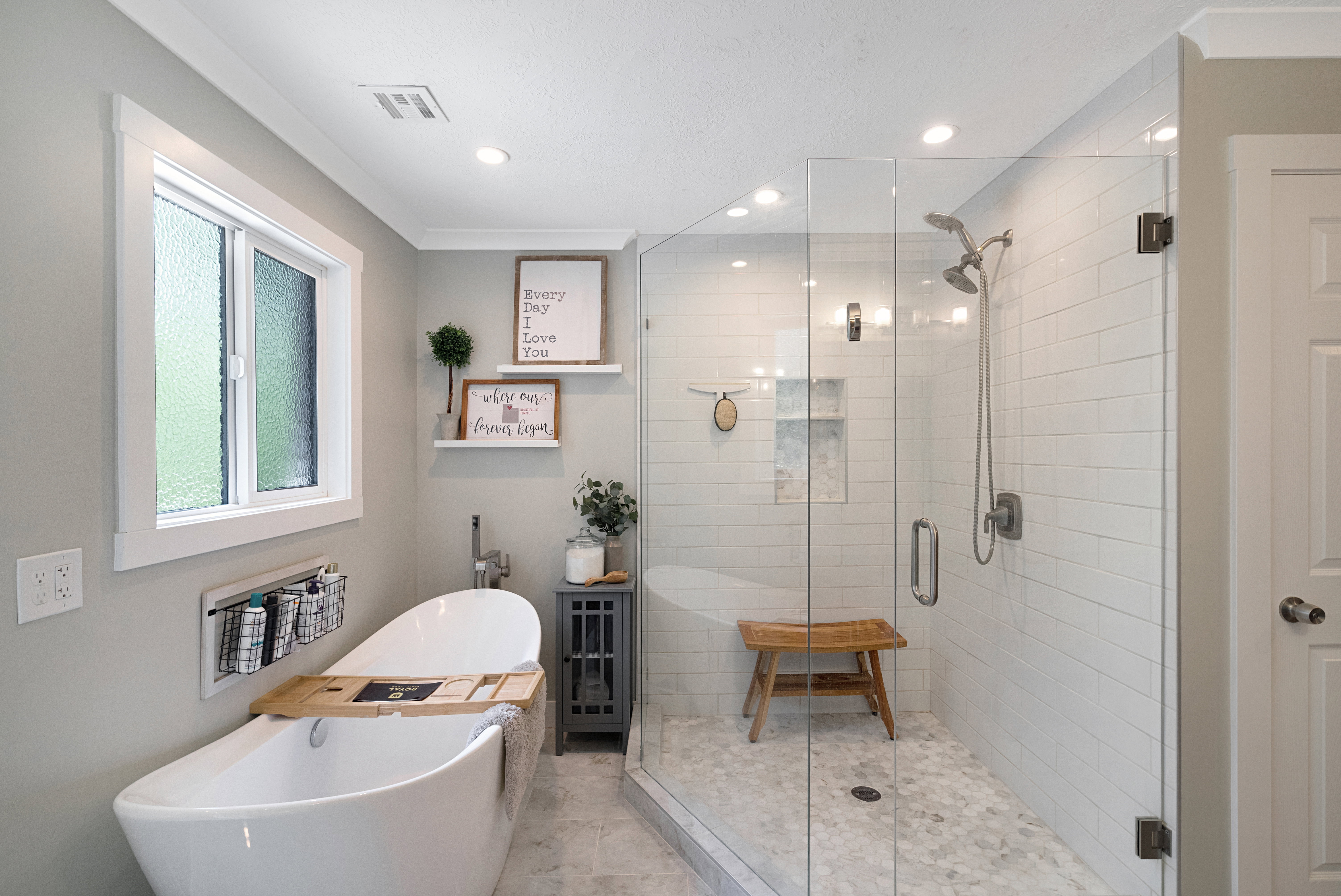 Freestanding soaking tub with a floor-mounted faucet, complemented by a separate glass-enclosed shower featuring subway tile walls and a hexagonal tile floor