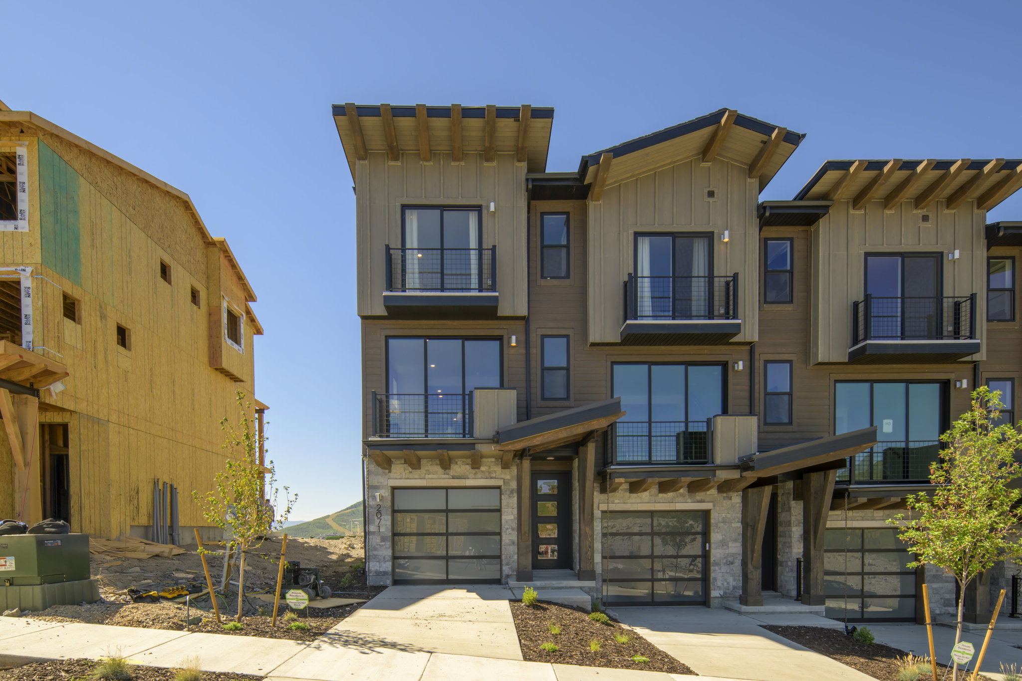 Contemporary townhome exterior featuring multi-level design, wood-look siding, stone accents, and multiple balconies with metal railings