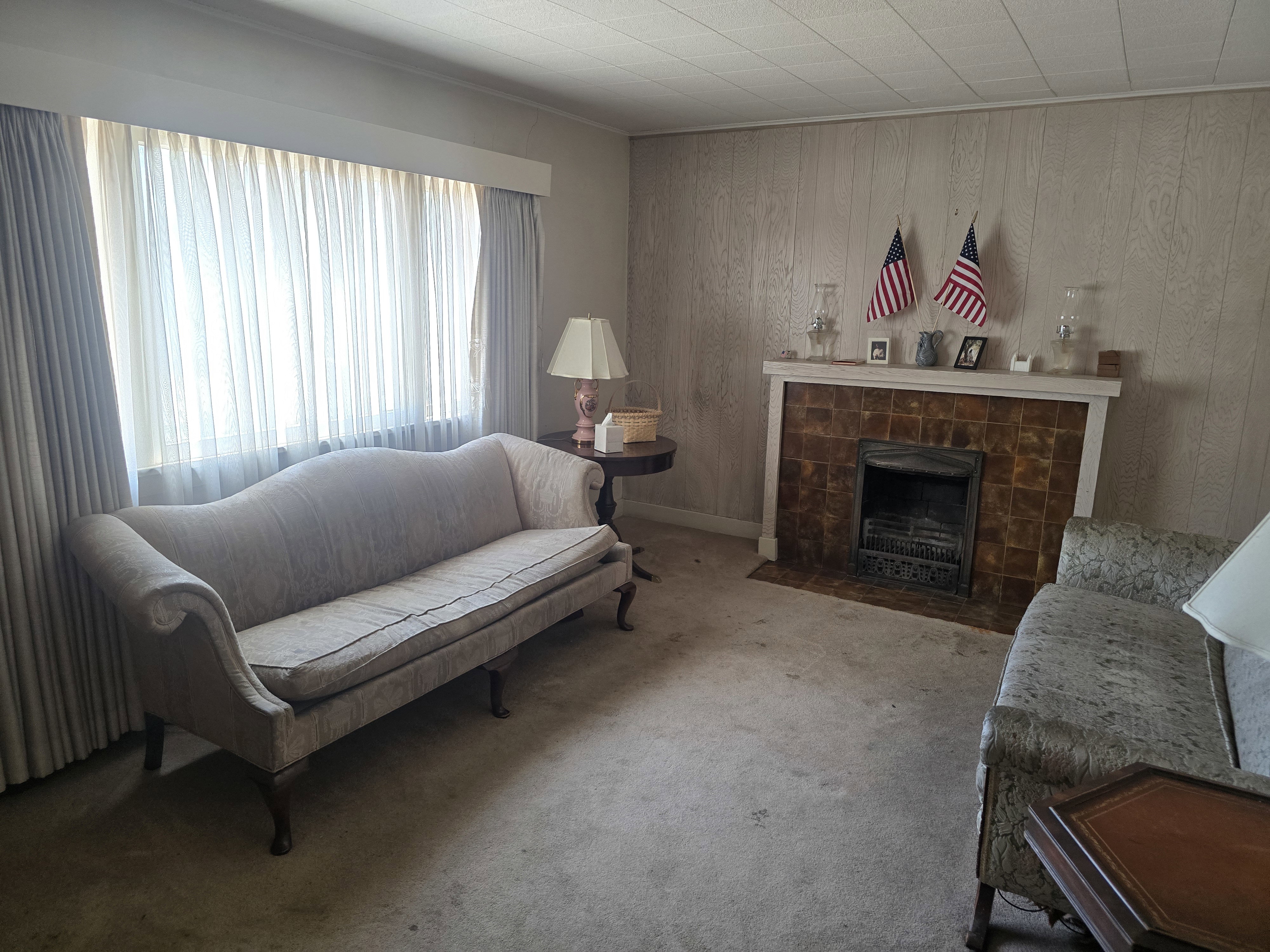 Living area featuring a tiled fireplace with a white mantel, wood-panel accent wall, and ceiling tiles
