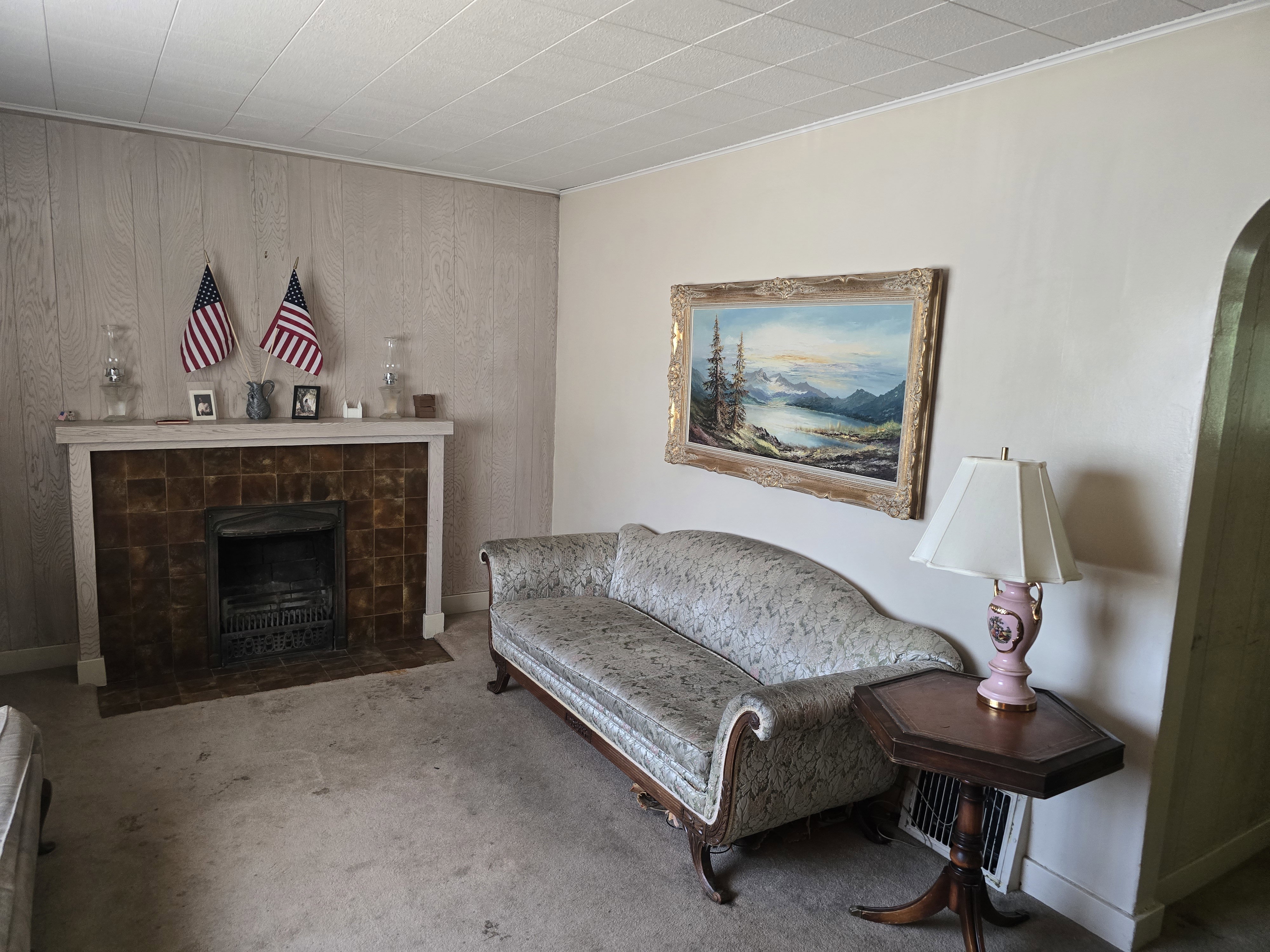 Living space featuring a tiled fireplace with a white mantel, wood paneling, and wall-to-wall carpeting