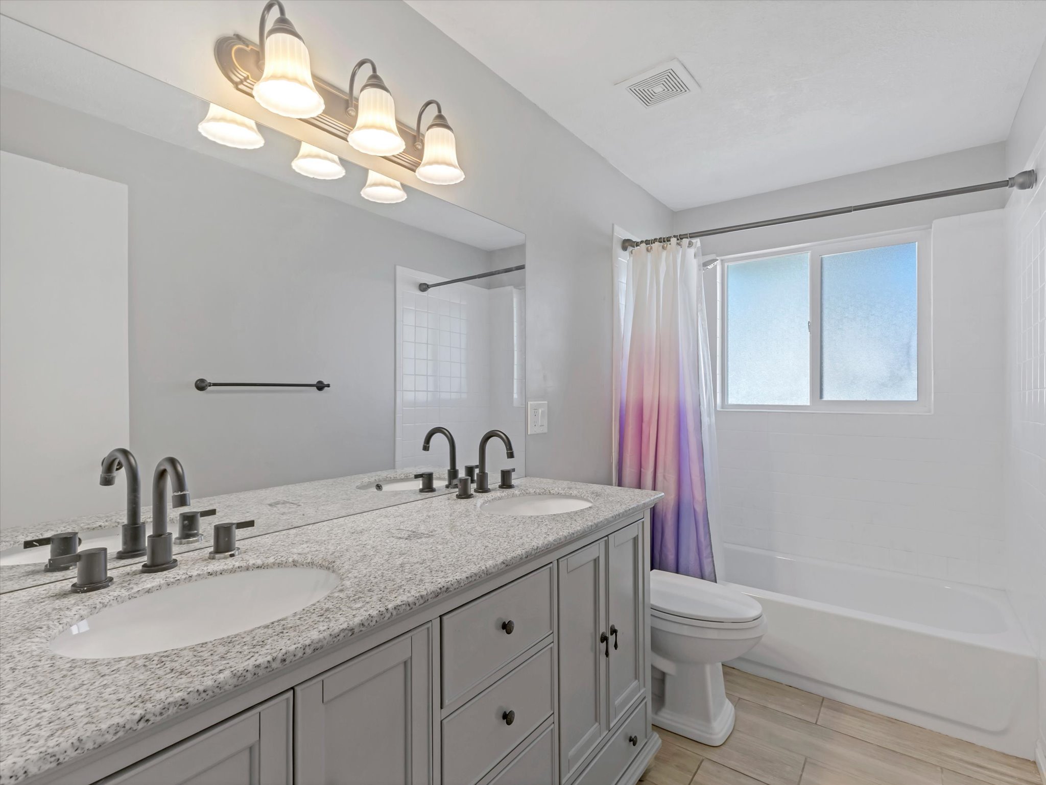 Bathroom featuring a dual vanity with a granite-style countertop, undermount sinks, and dark-toned hardware