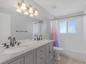 Bathroom featuring a dual vanity with a granite-style countertop, undermount sinks, and dark-toned hardware