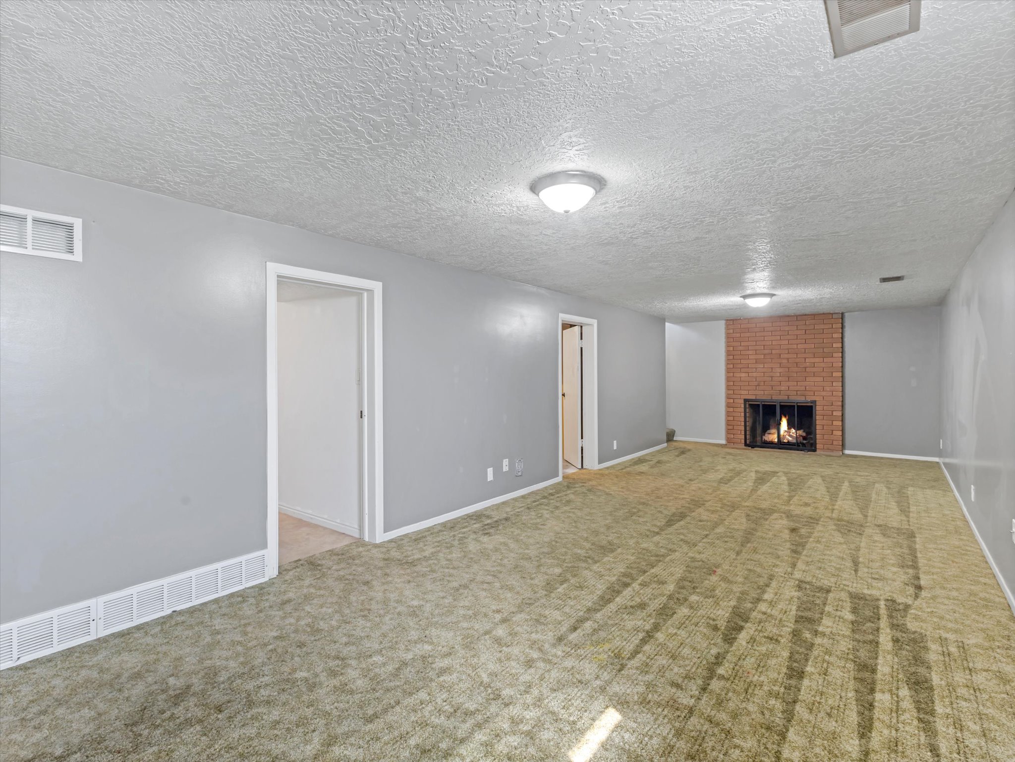 Spacious room with plush carpeting, featuring a brick-surround fireplace