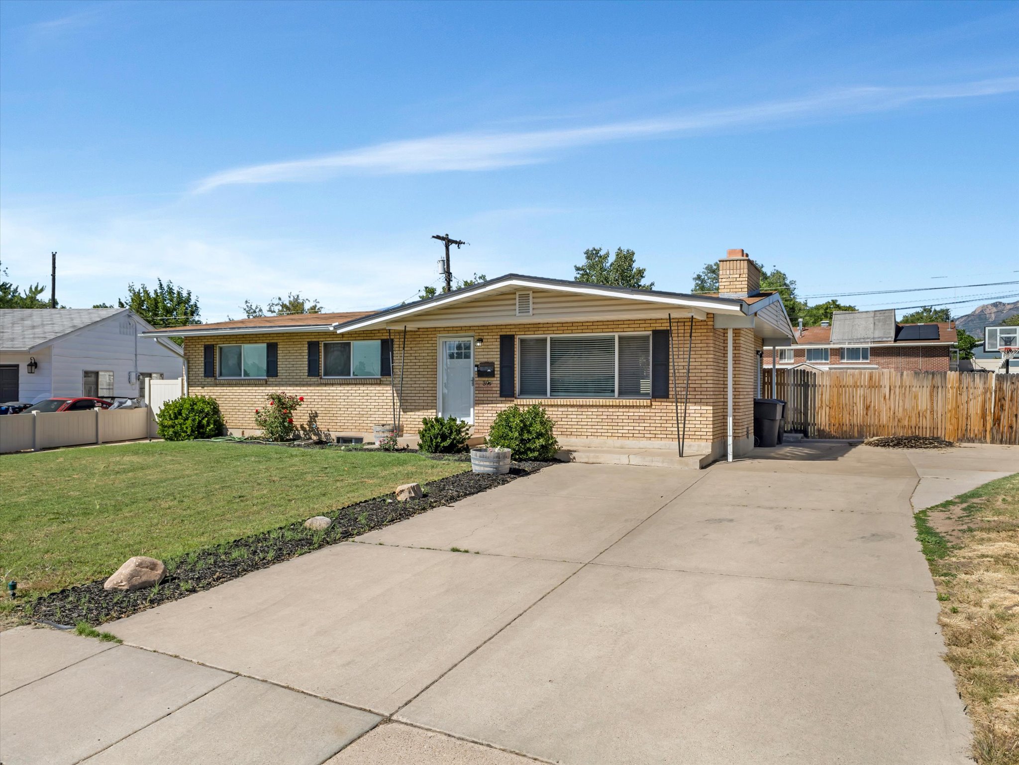Ranch-style exterior featuring brick siding, a concrete driveway, a manicured lawn, and mature landscaping