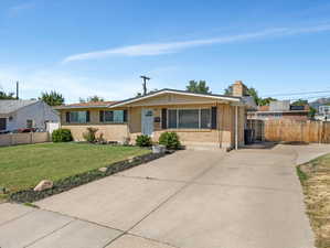 Ranch-style exterior featuring brick siding, a concrete driveway, a manicured lawn, and mature landscaping