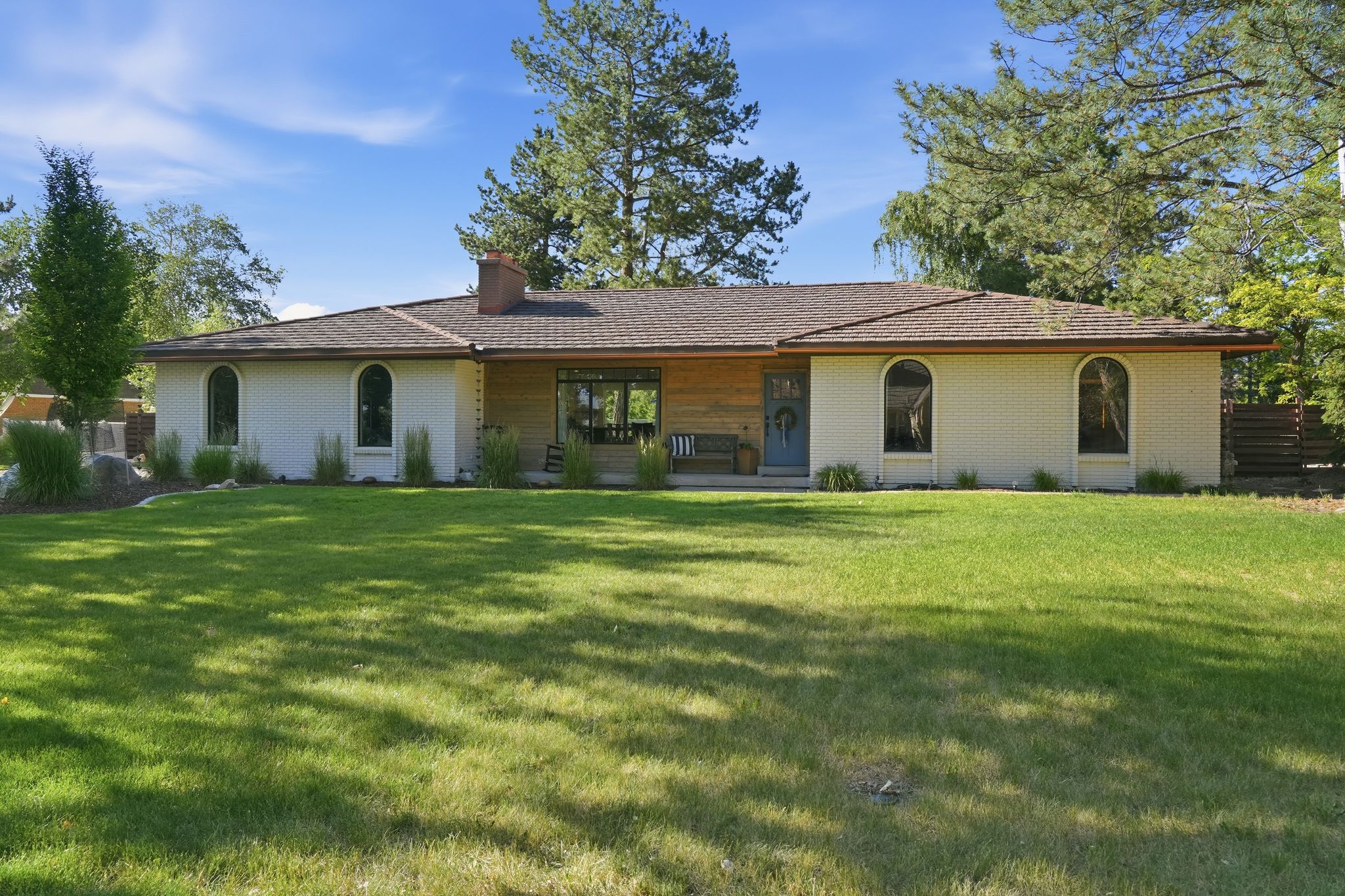Ranch-style exterior with a brown shingle roof, white brick façade, and arched windows