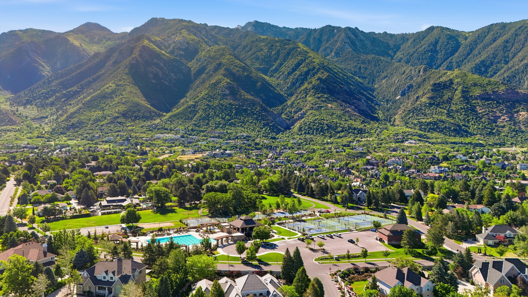 Expansive community featuring mature trees, a swimming pool, multiple tennis courts, and a mountainous backdrop