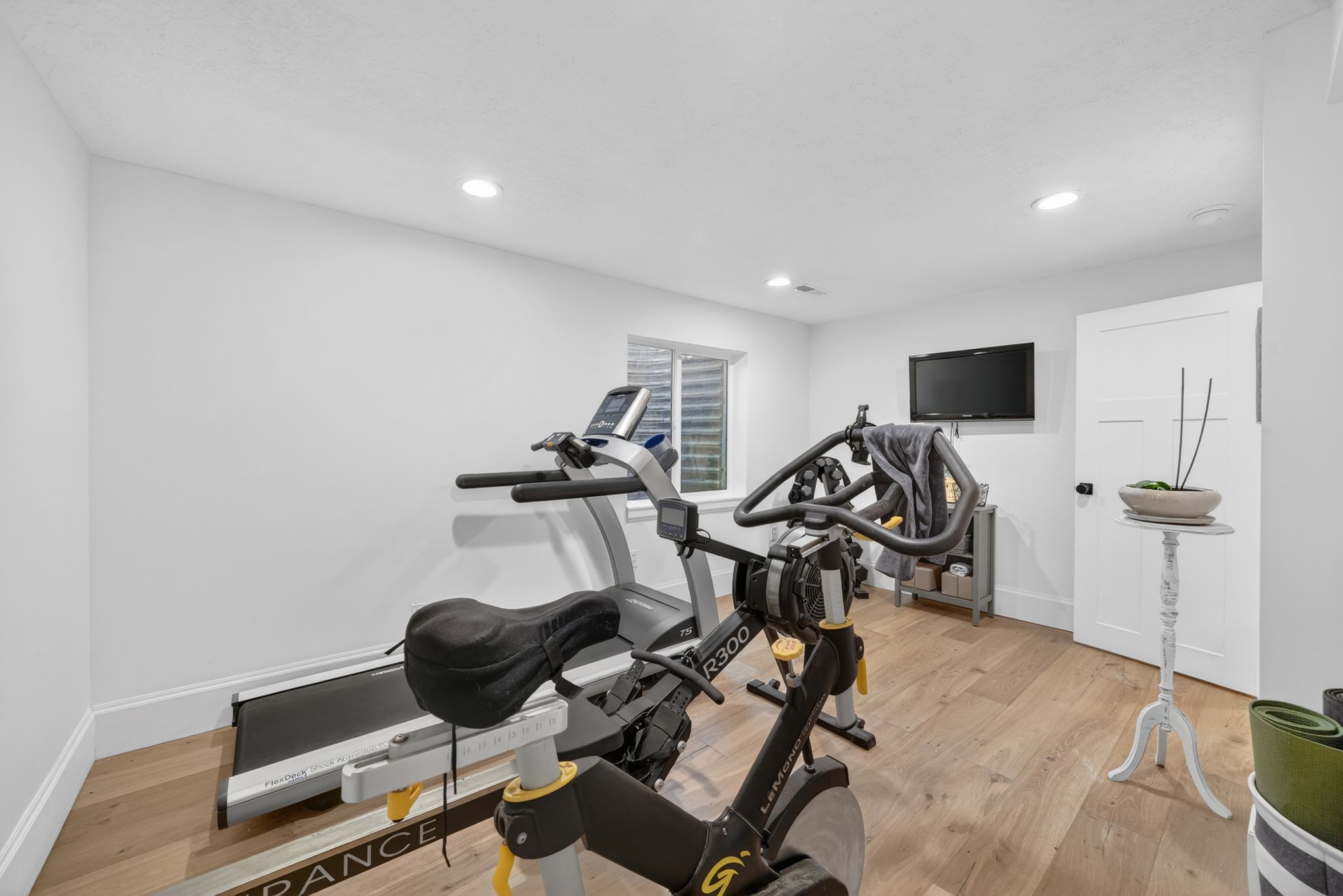 Spacious room with light wood-finish flooring, recessed lighting, and a white paneled door