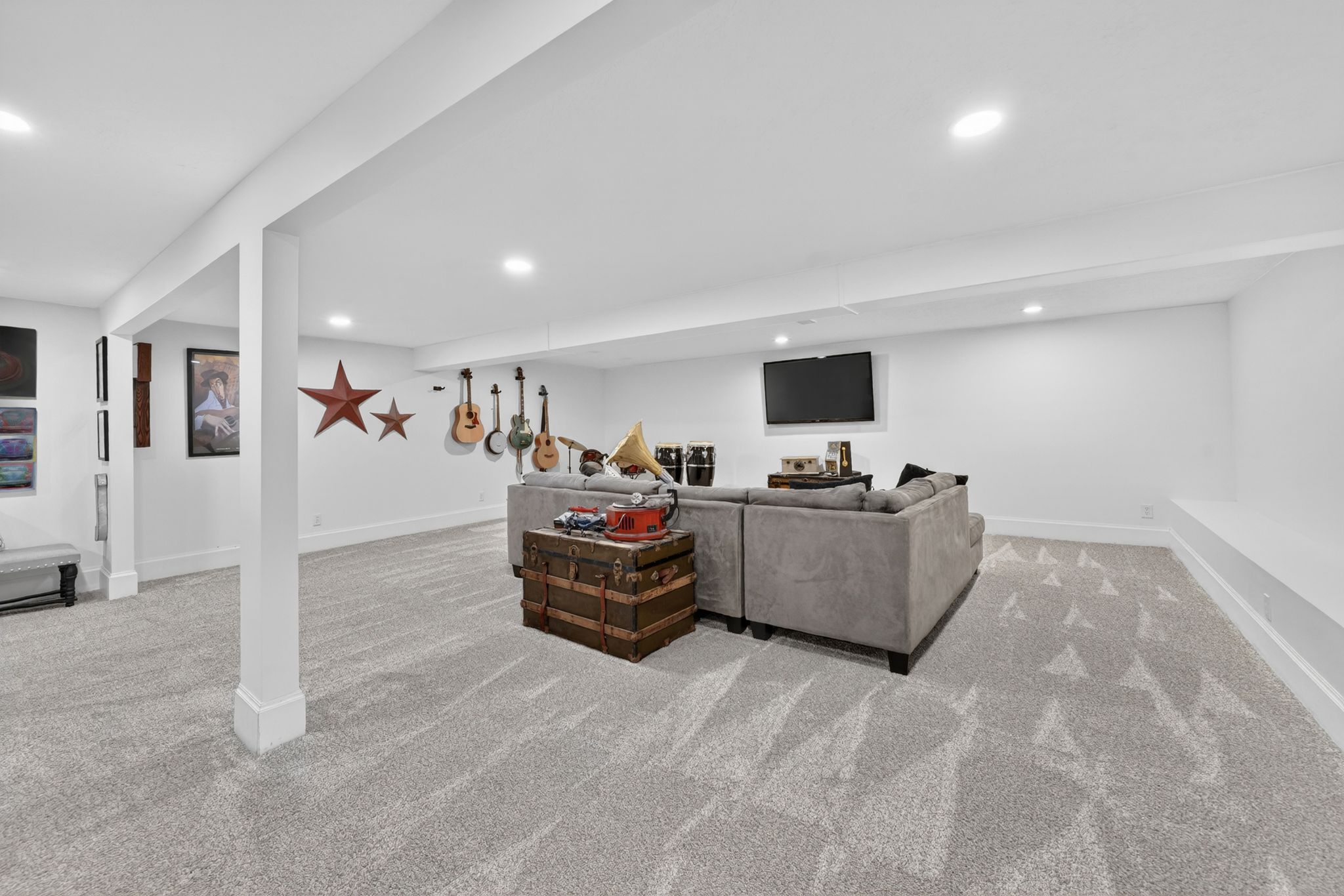 Spacious finished basement featuring recessed lighting, light-toned patterned carpeting, crisp white walls, and a built-in wall bench