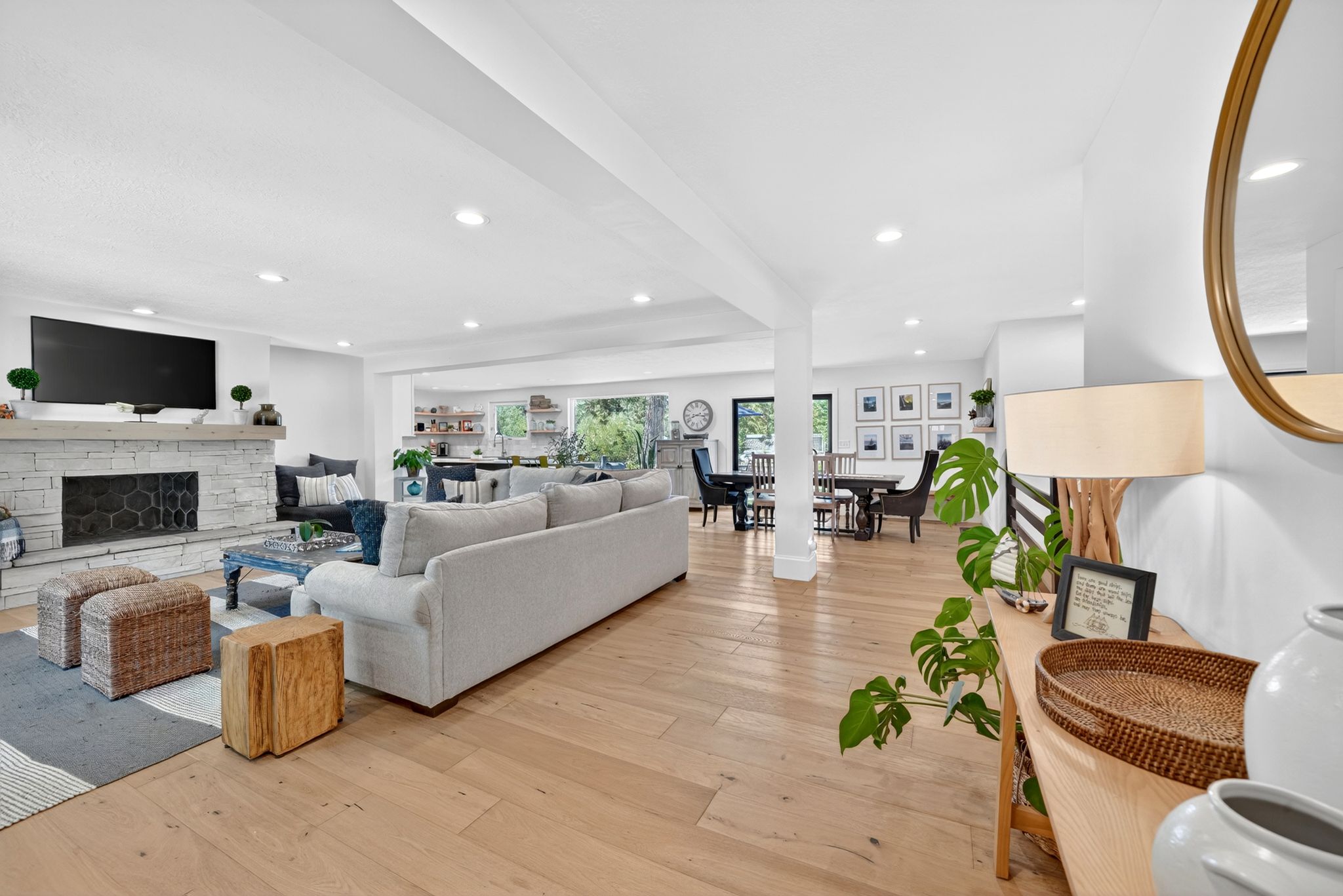 Spacious living area featuring light wood-finish flooring, a stacked stone fireplace, recessed lighting, and white walls