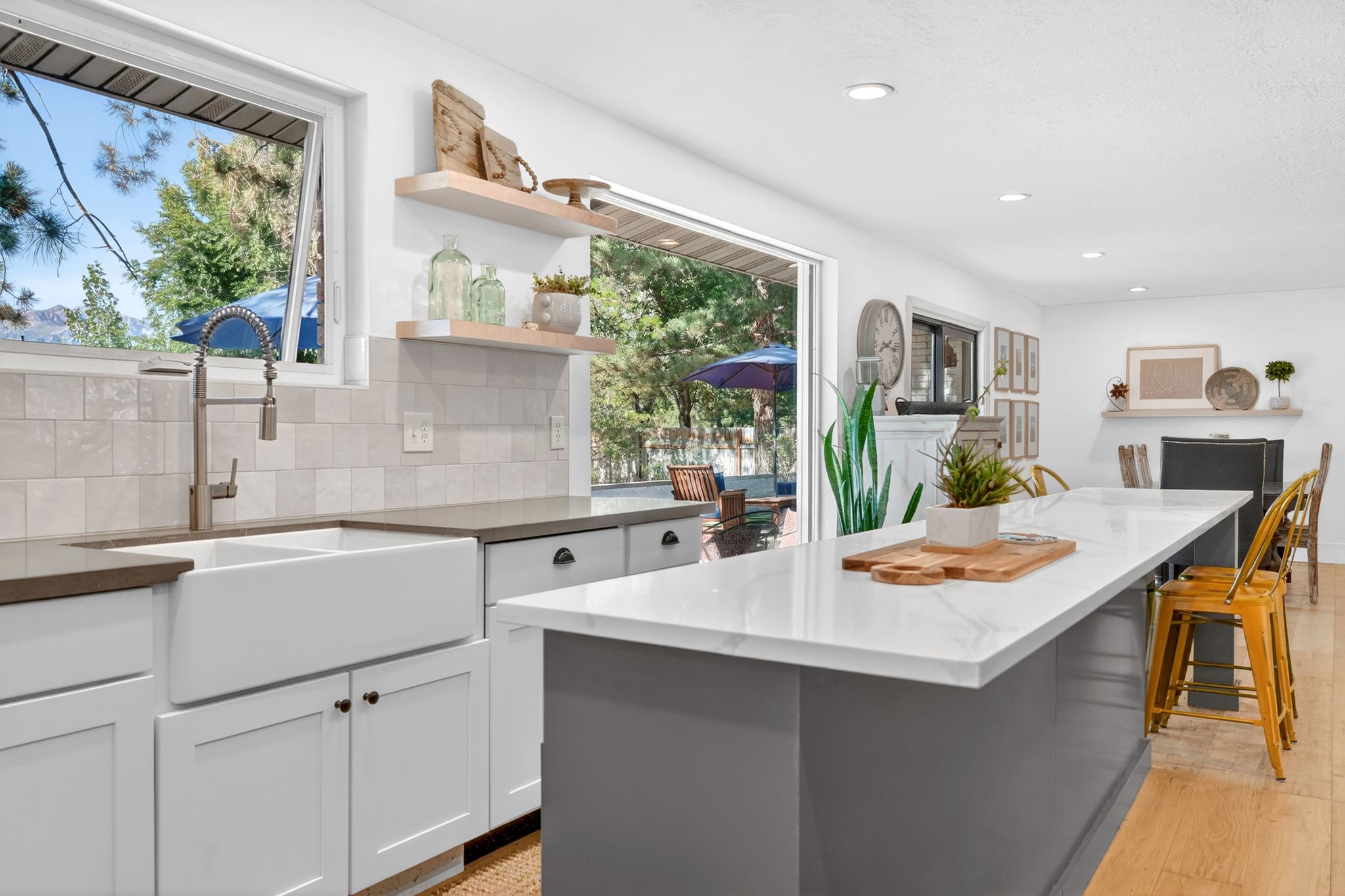 Bright kitchen featuring white shaker cabinetry, an apron-front sink, light-toned tiled backsplash, and a spacious island with a white countertop