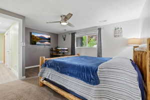 Carpeted room featuring a ceiling fan with integrated lighting, a wall-mounted television, and a window with drapes