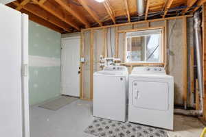 Laundry area featuring exposed ceiling joists and concrete flooring, a white window with blinds, and existing plumbing and electrical conduit