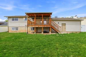 Rear exterior featuring a large wooden deck with stairs to the yard, vinyl siding, multiple windows, and a ground-level access door