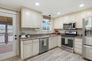 Kitchen with light wood-finish cabinetry, stainless steel appliances, wood-finish flooring, recessed lighting, and direct patio access