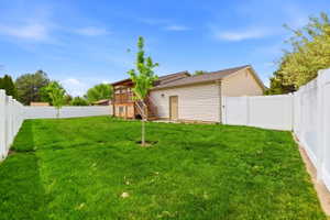 Expansive lawn area enclosed by white vinyl fencing, featuring a multi-level wood deck and a ground-level exterior door