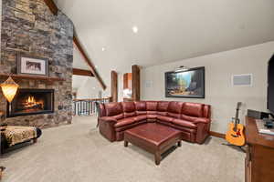 Living room with lofted ceiling with beams, light colored carpet, a stone fireplace, and recessed lighting