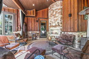Living area with an outdoor stone fireplace, wood walls, recessed lighting, and a vaulted wood ceiling