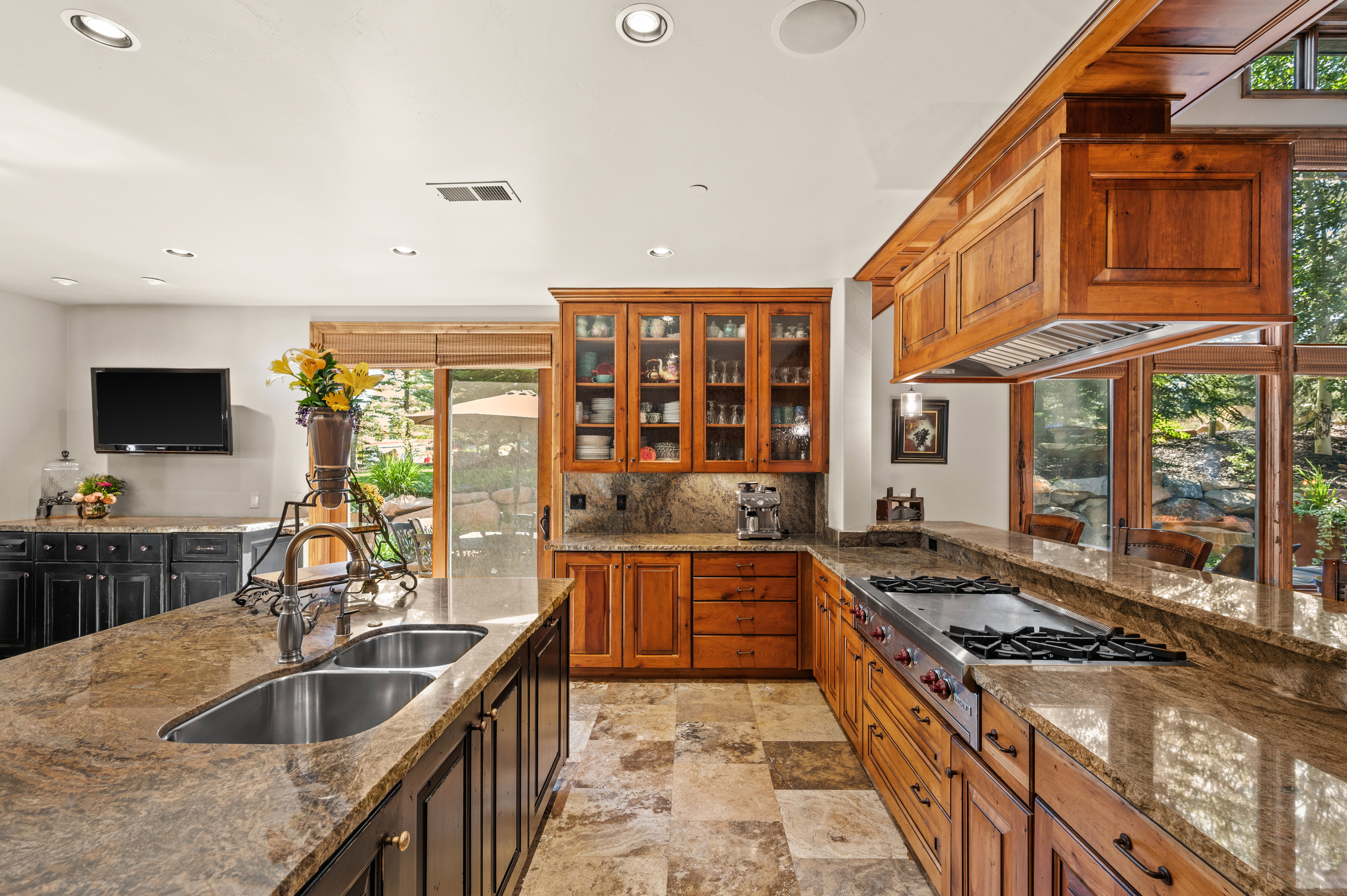 Kitchen featuring dark stone countertops, stainless steel gas cooktop, glass insert cabinets, light stone finish floors, and recessed lighting