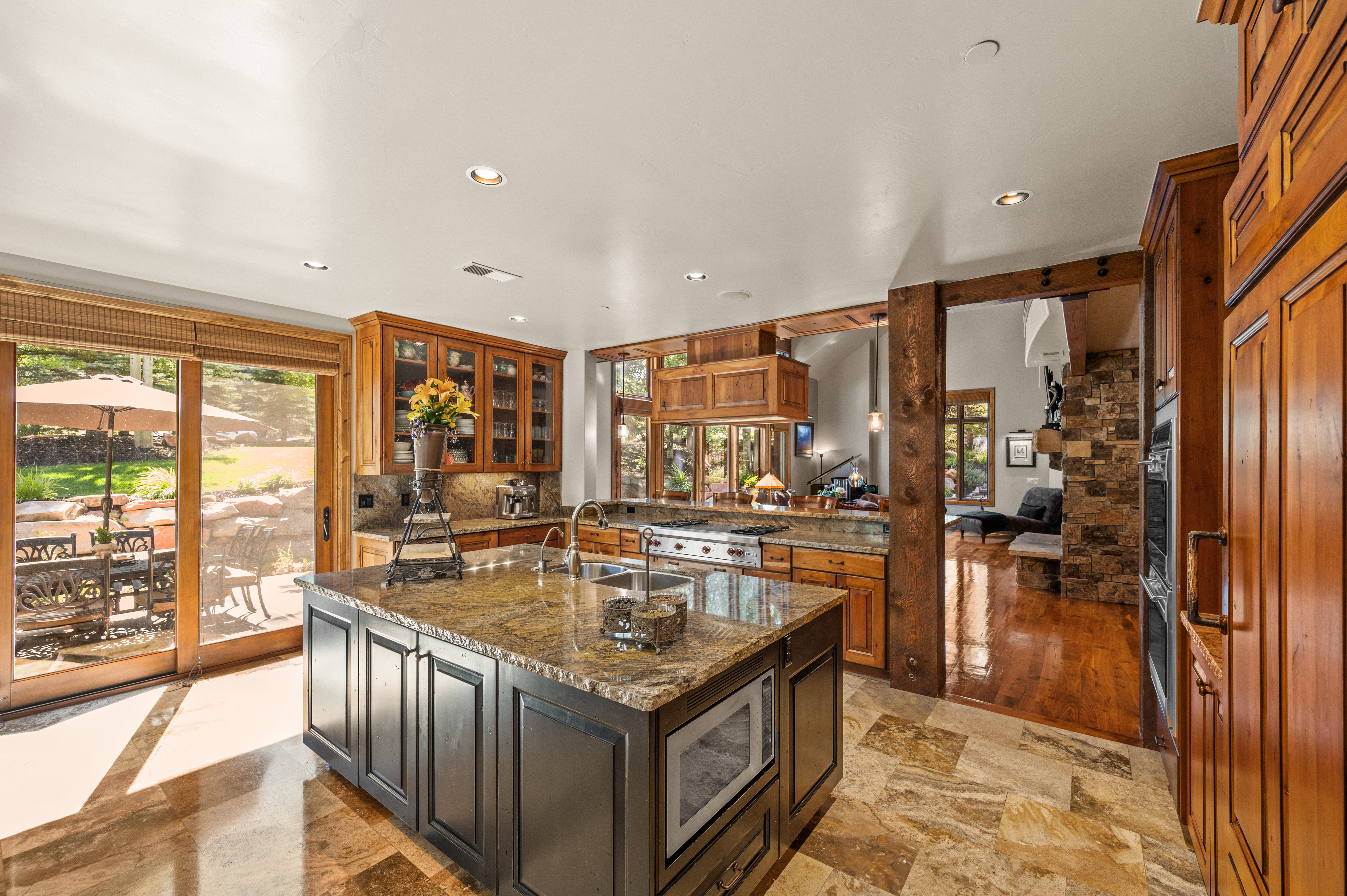 Kitchen featuring dark stone counters, glass insert cabinets, recessed lighting, a kitchen island with sink, and stainless steel appliances