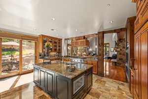 Kitchen featuring dark stone counters, glass insert cabinets, recessed lighting, a kitchen island with sink, and stainless steel appliances