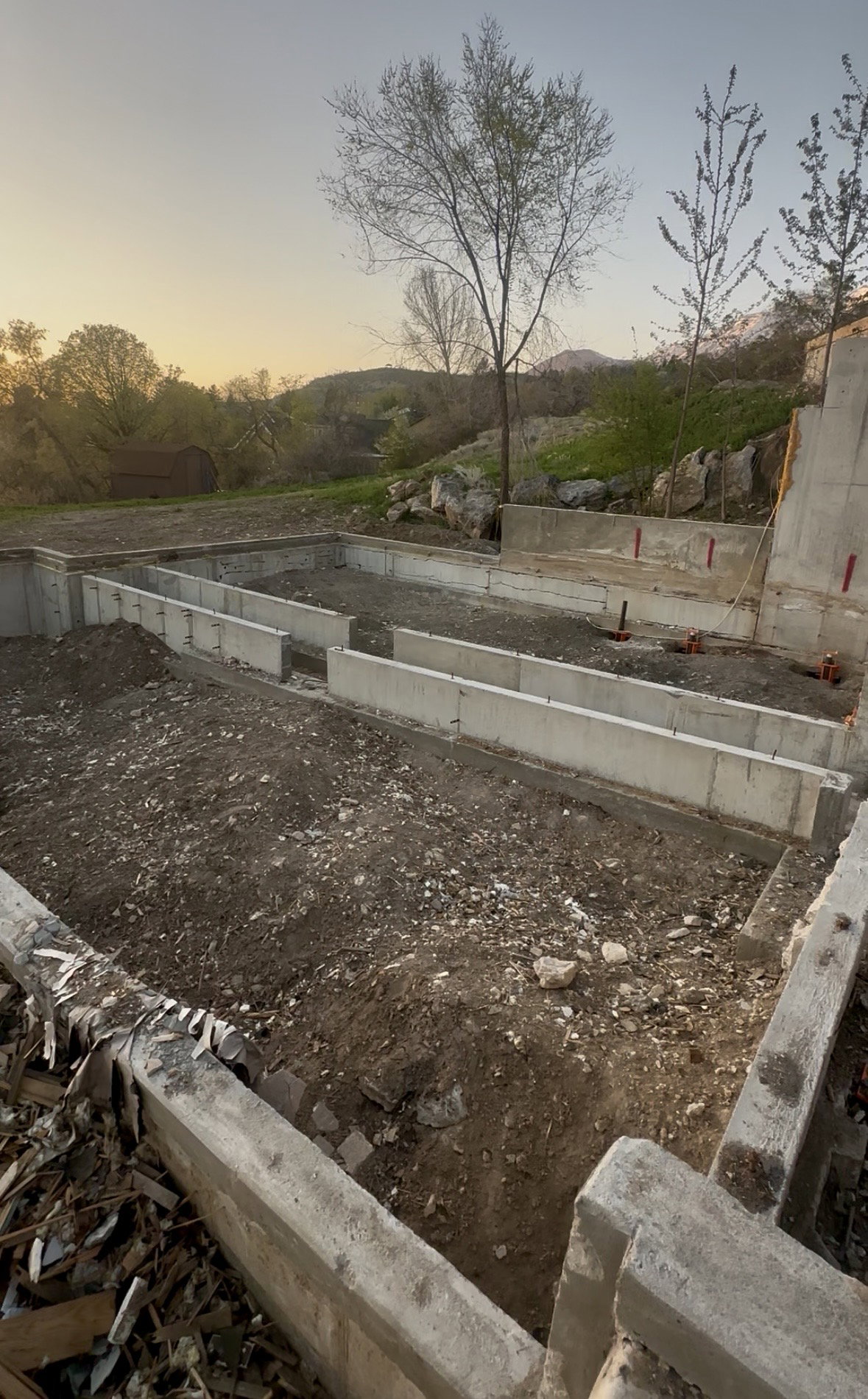 Concrete foundation footings with a tiered retaining wall, set against a backdrop of distant hills and mature trees
