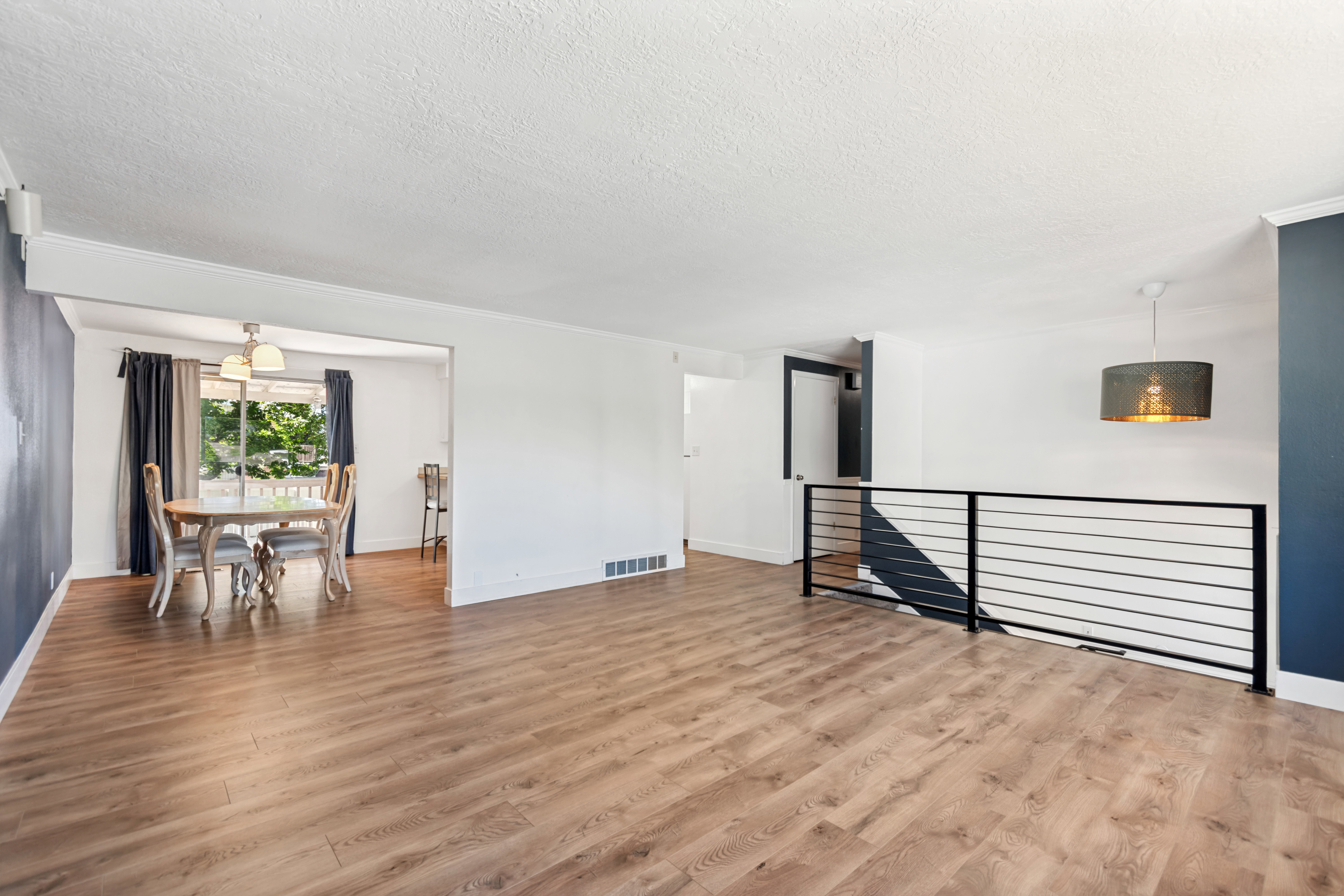 Expansive living area featuring wood-finish flooring, a contemporary black horizontal bar railing, and a modern drum pendant light fixture