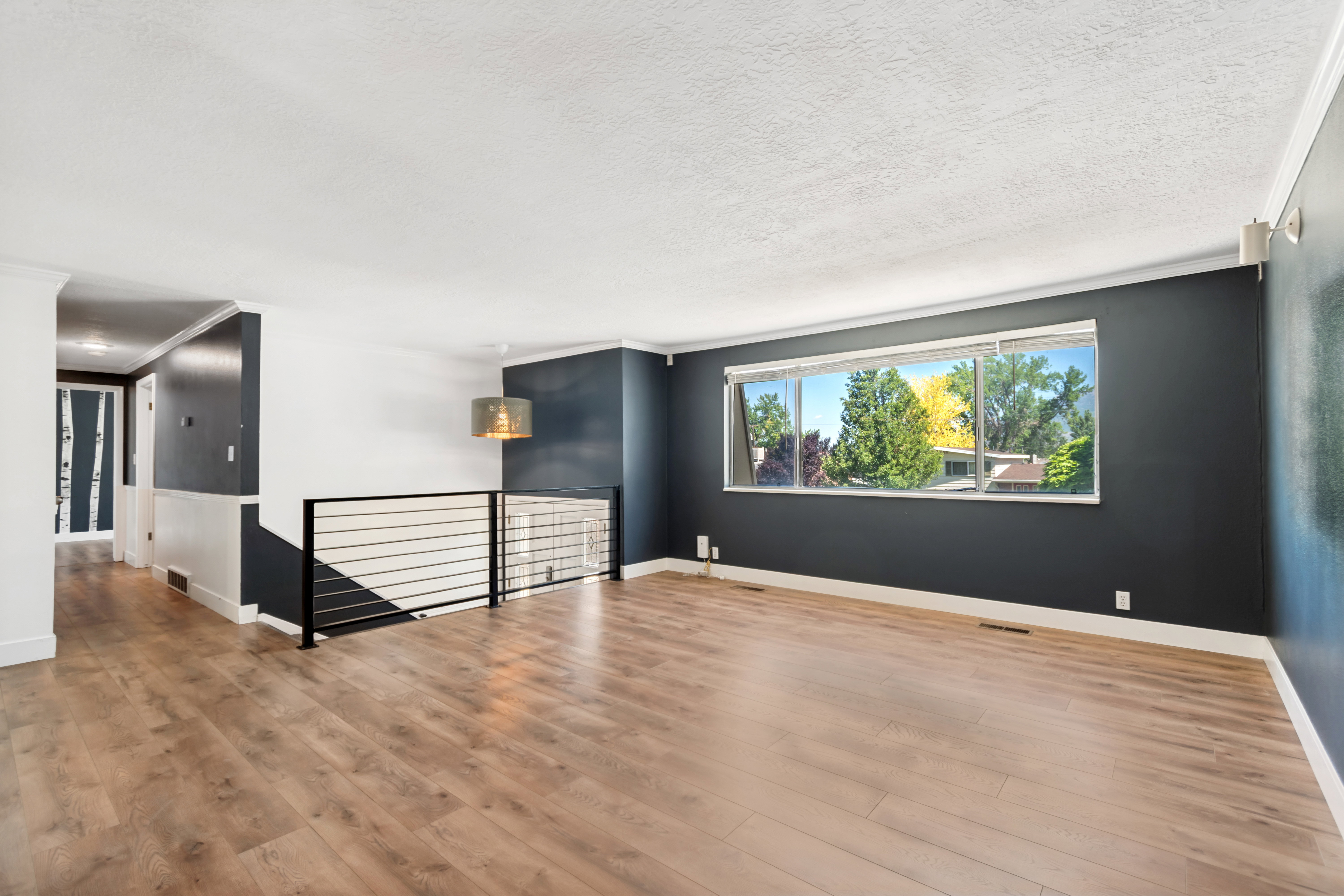 Bright living area featuring wood-finish flooring, a contemporary horizontal bar railing, a large picture window, and a modern drum pendant light fixture