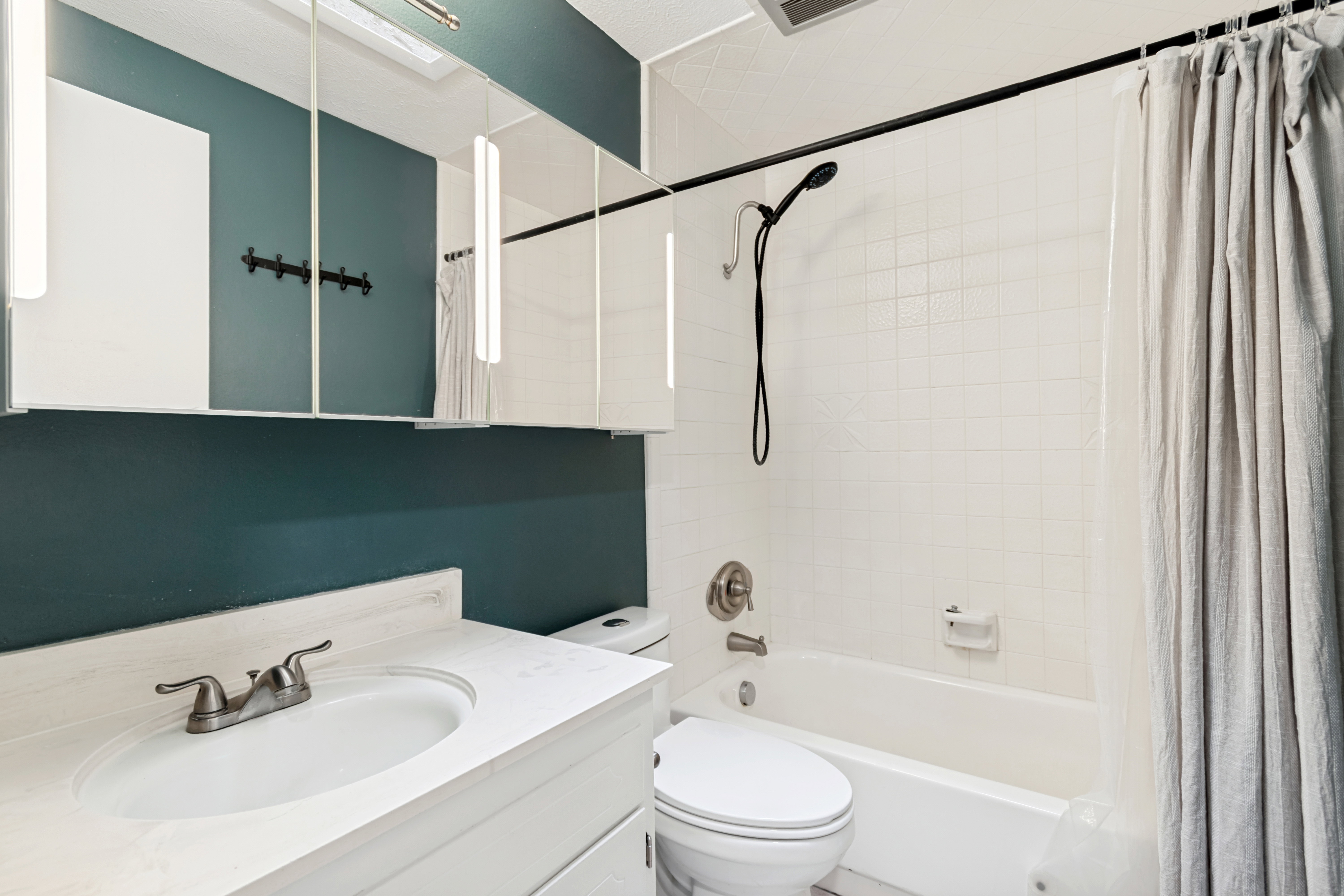 Bathroom vanity with an integrated sink and brushed nickel faucet, complemented by a large mirrored medicine cabinet, &  sky light