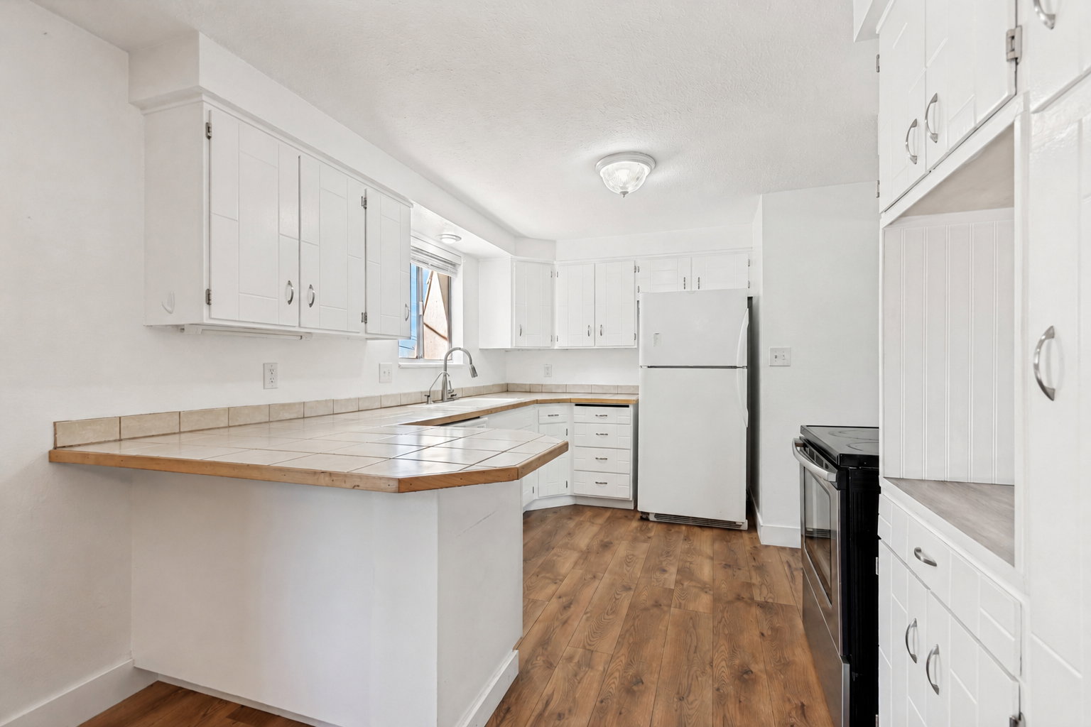 Kitchen featuring extensive white cabinetry, wood-finish flooring, and a peninsula with a tile countertop