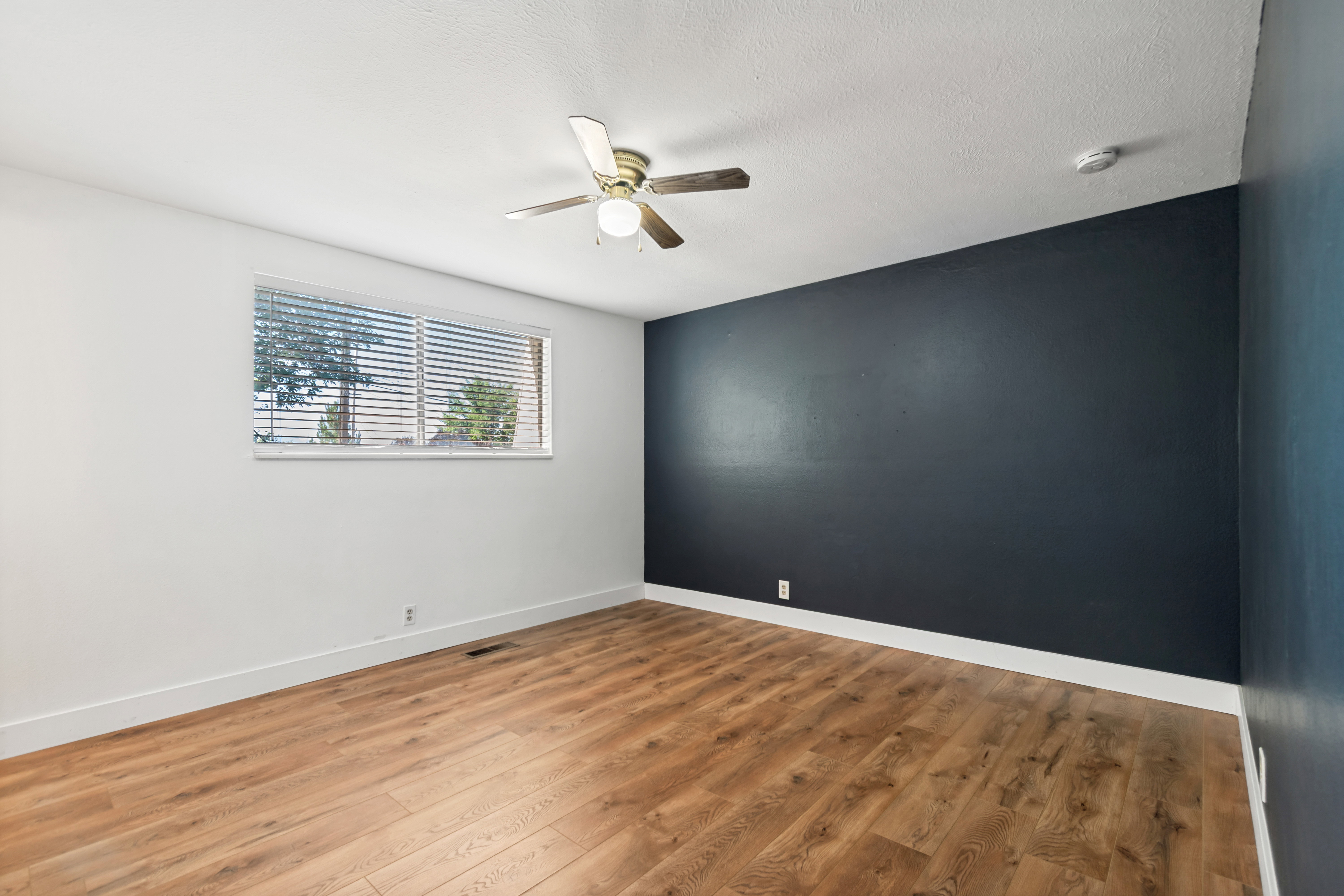 Room featuring wood-finish flooring, a ceiling fan with integrated lighting, and a window with horizontal blinds