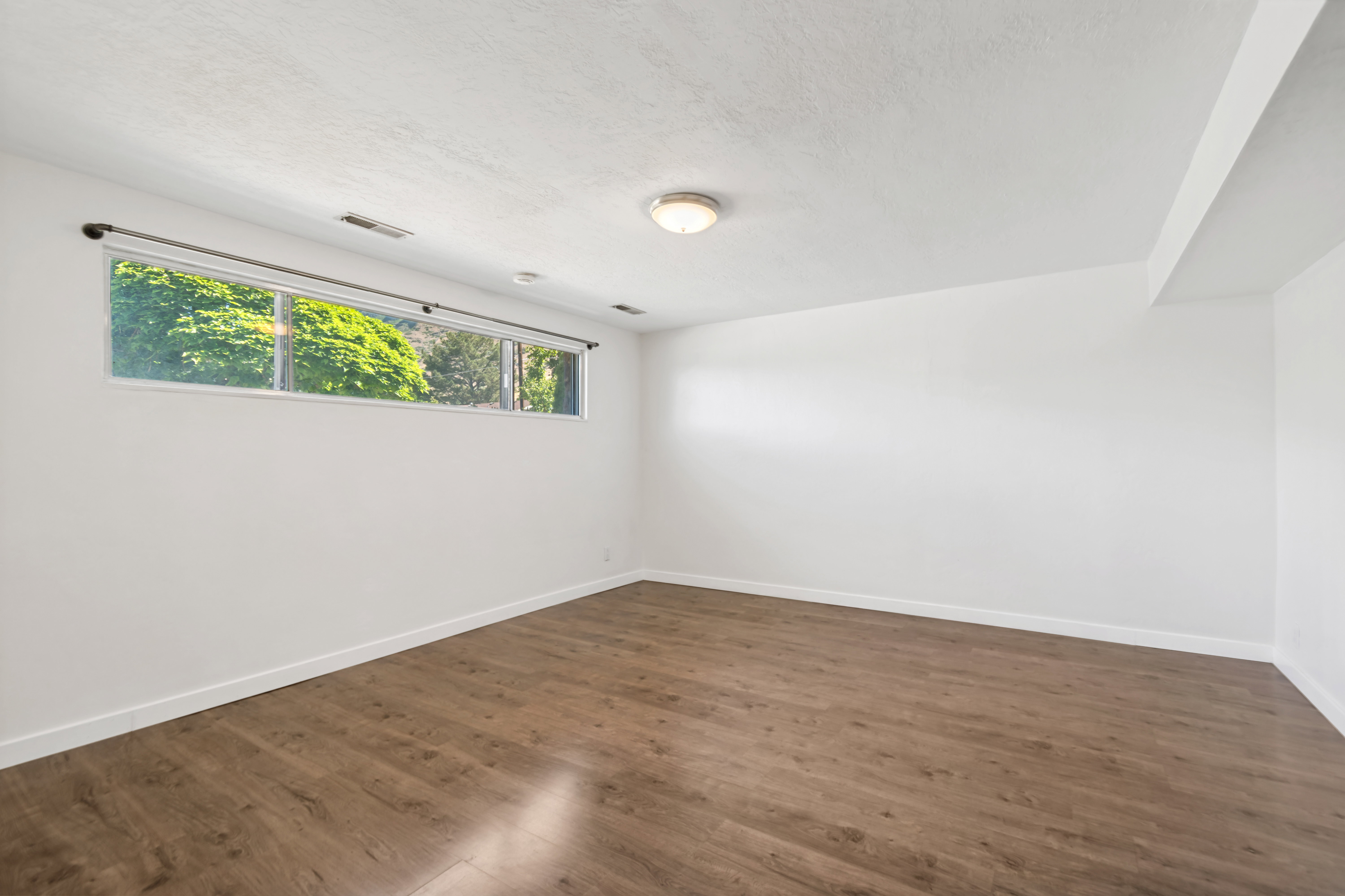 Spacious room featuring daylight window, wood-finish flooring and a neutral color palette