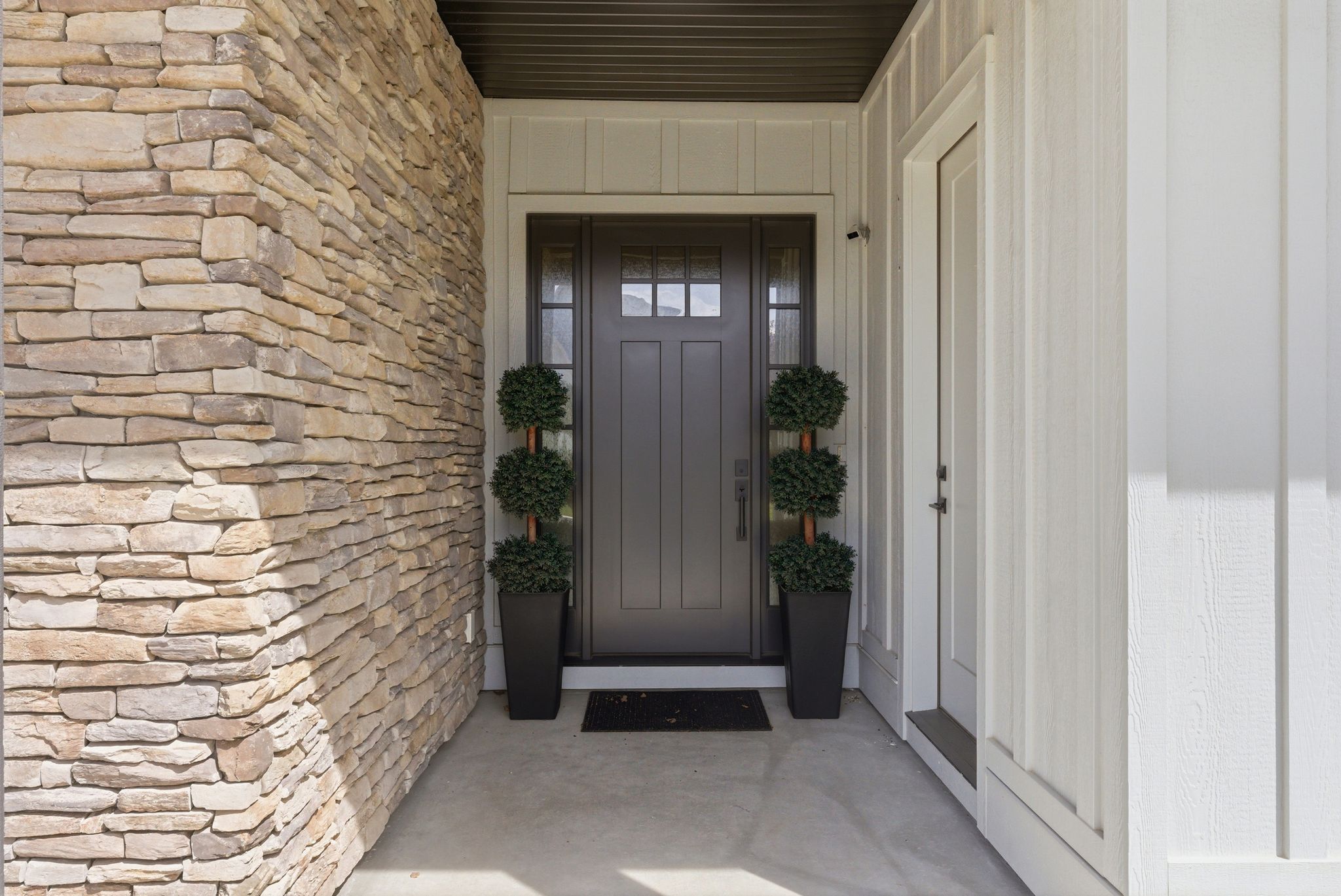 Entryway featuring a dark paneled door with glass inserts, flanked by stone veneer and board and batten siding