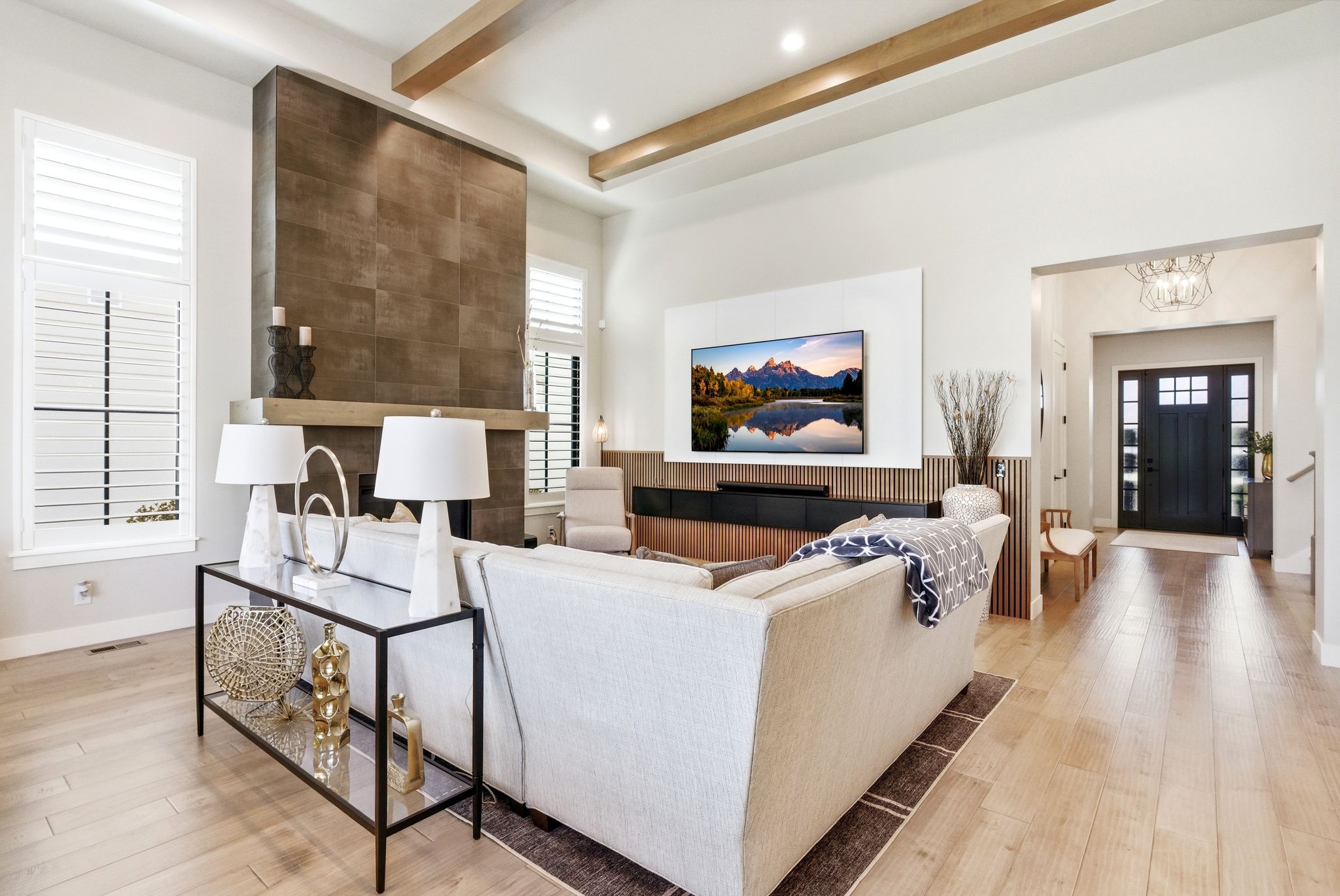 Spacious living area featuring a floor-to-ceiling tiled fireplace, high ceilings with exposed wood beams, and large windows with plantation shutters