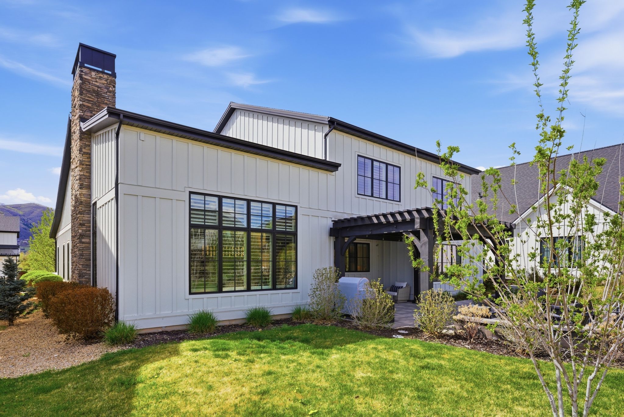 Contemporary white board-and-batten siding with a dark trim and a stone chimney