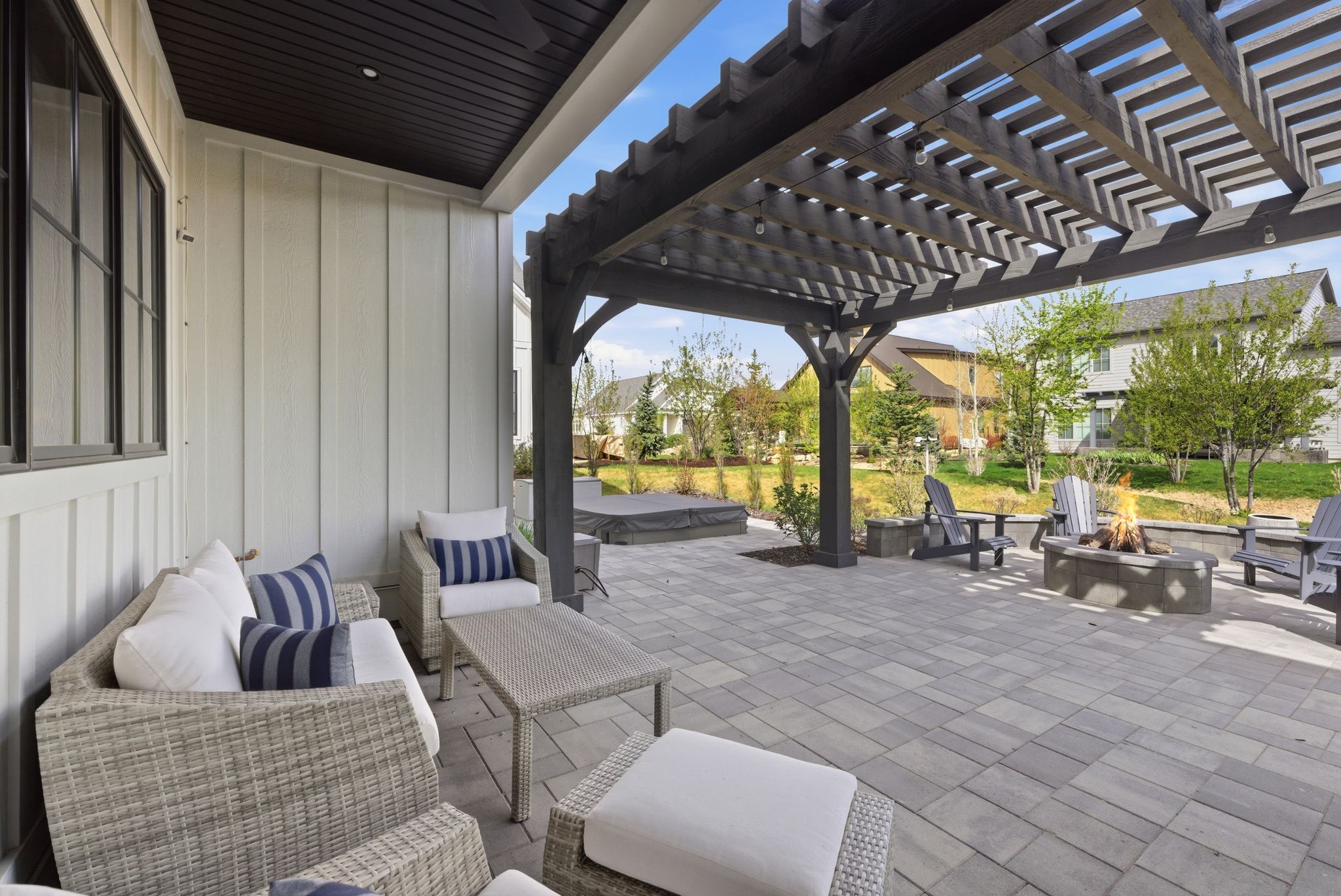 Expansive paver patio with a built-in fire pit, covered pergola structure, and a board and batten exterior wall