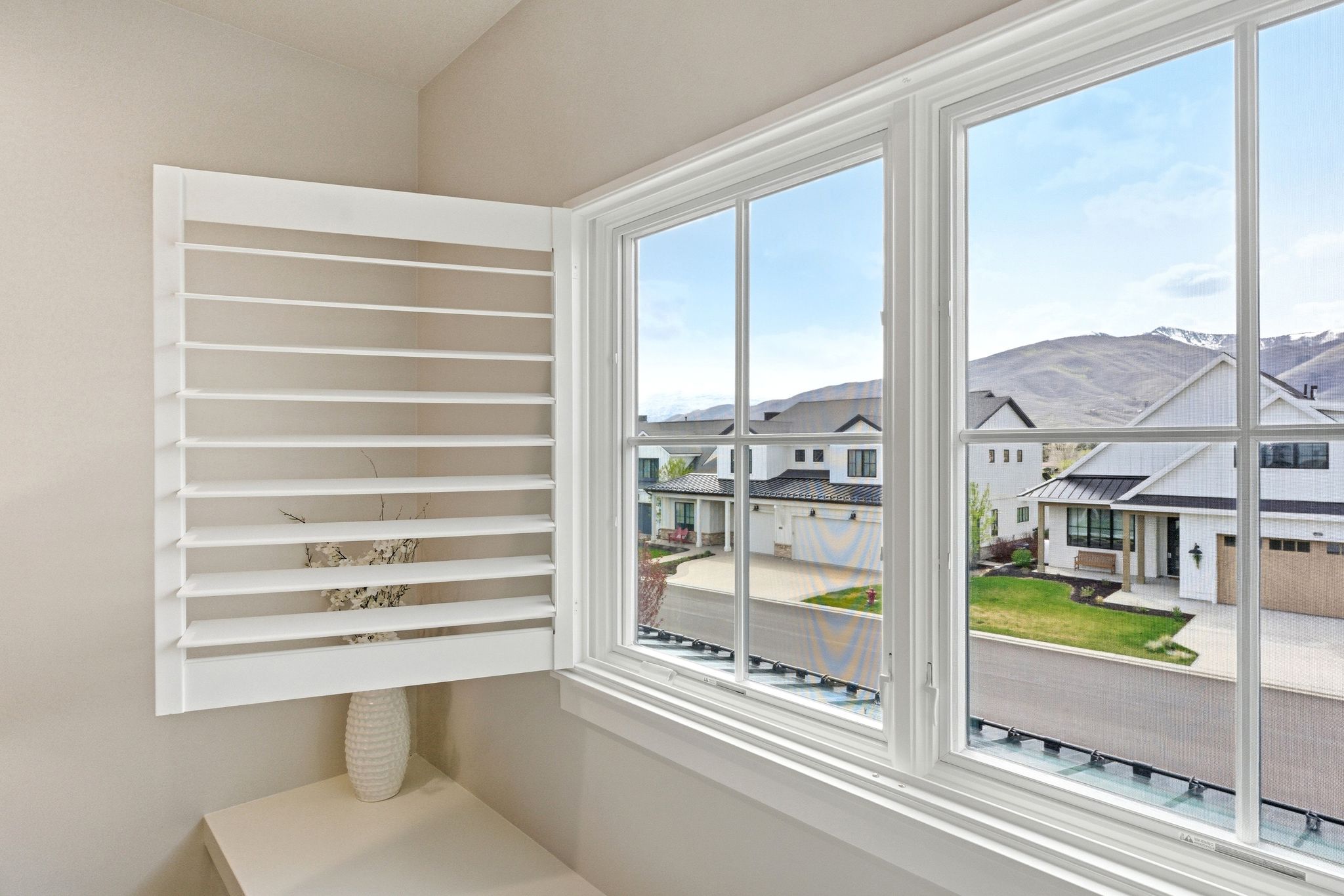 Window with white grid panes and plantation shutters, offering a mountain backdrop