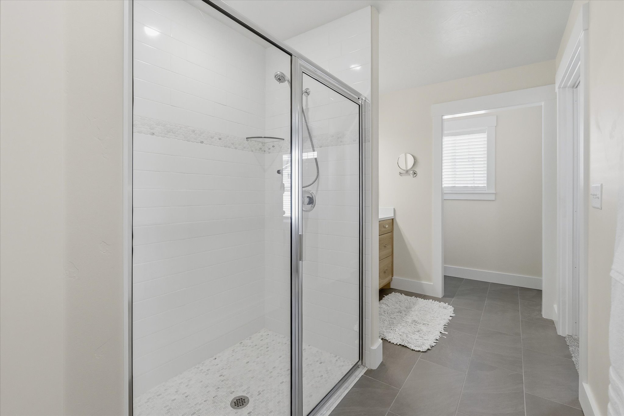 Glass-enclosed shower with white subway tile, a mosaic accent band, and a pebble-finish shower pan