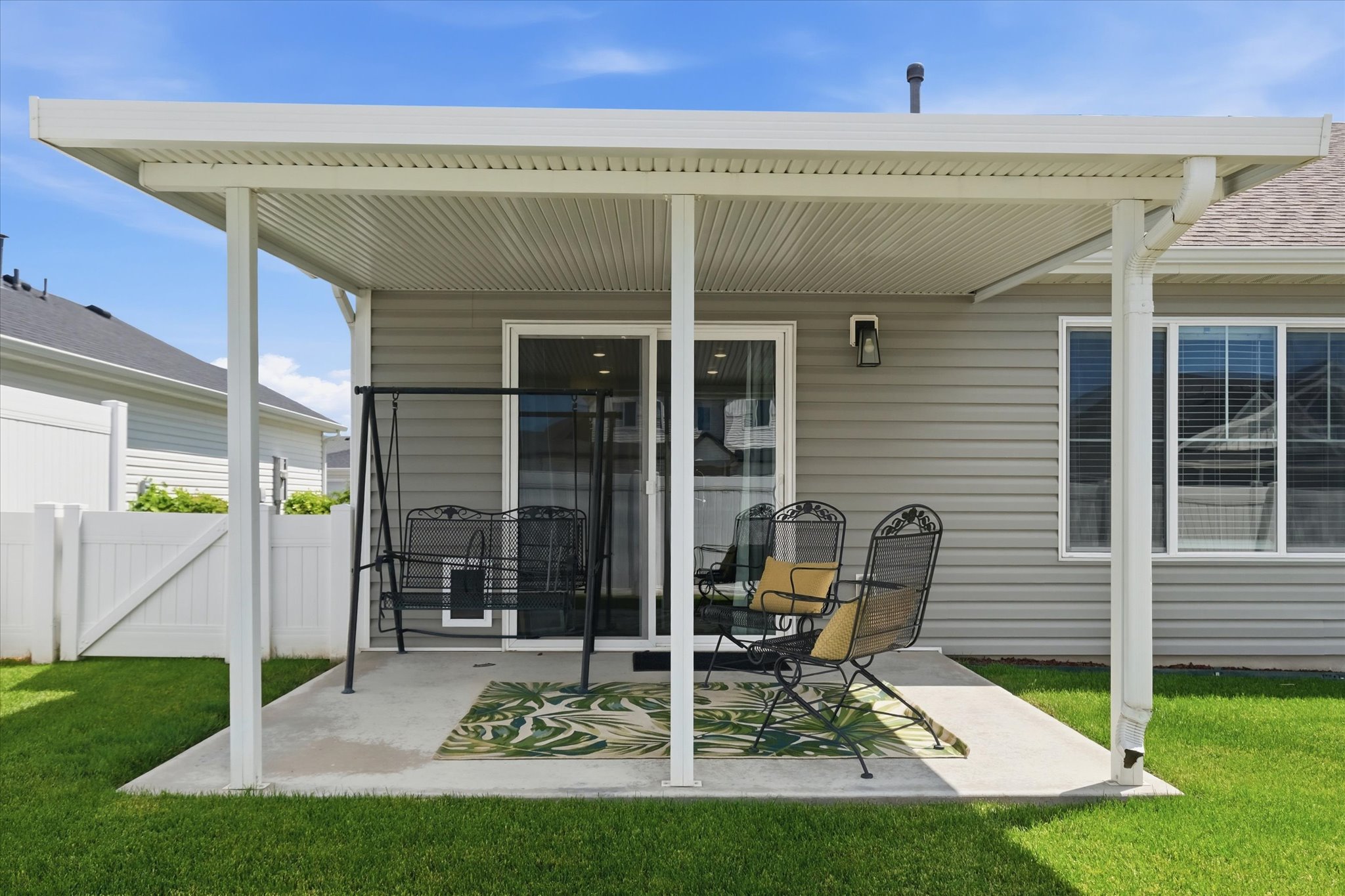 Covered concrete patio featuring a white pergola structure with integrated gutters, direct access through sliding glass doors, and a permanent wall-mounted exterior light fixture