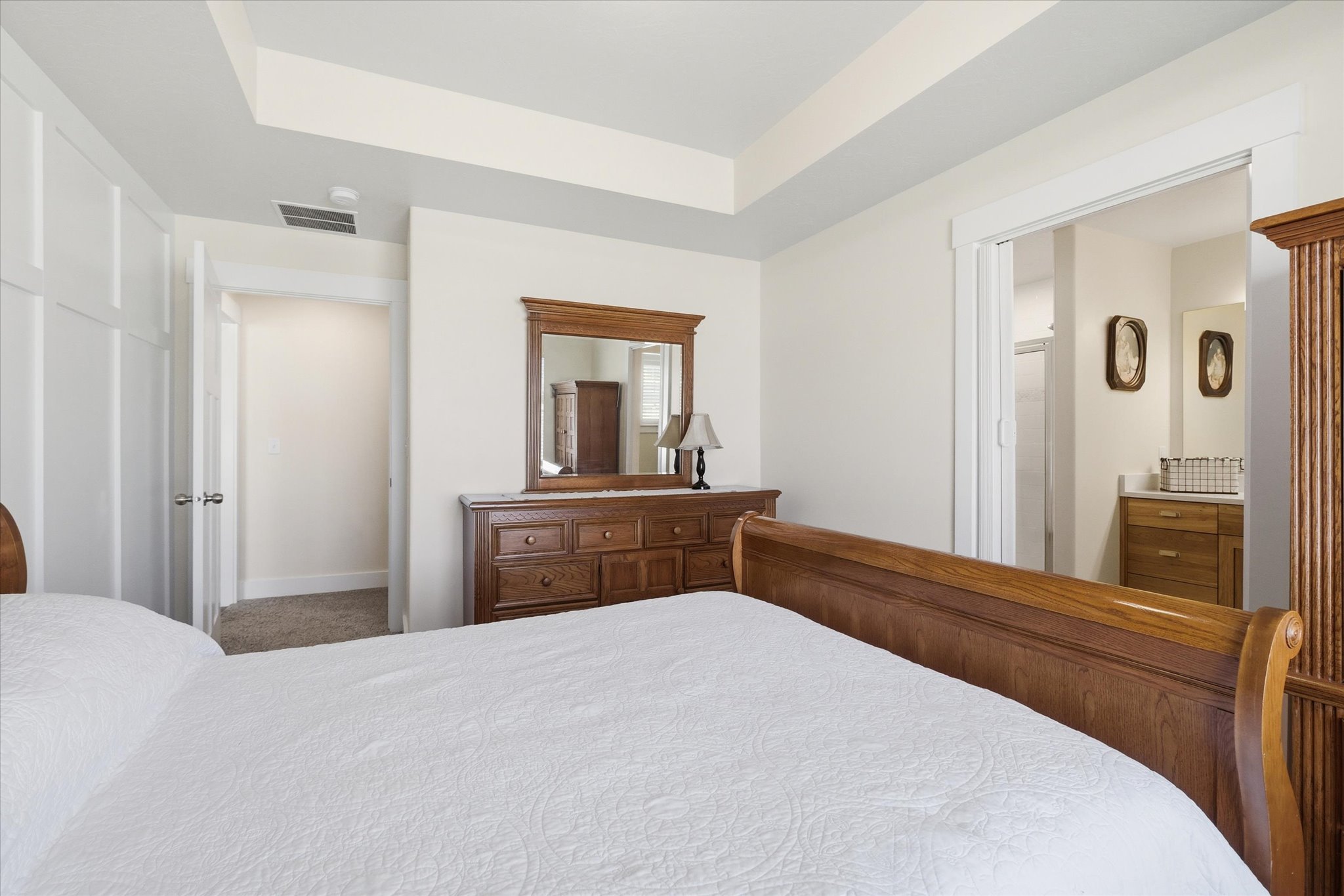 Tray ceiling with recessed lighting, white paneled wall detailing, light-toned carpeting, and a doorway opening to an additional space