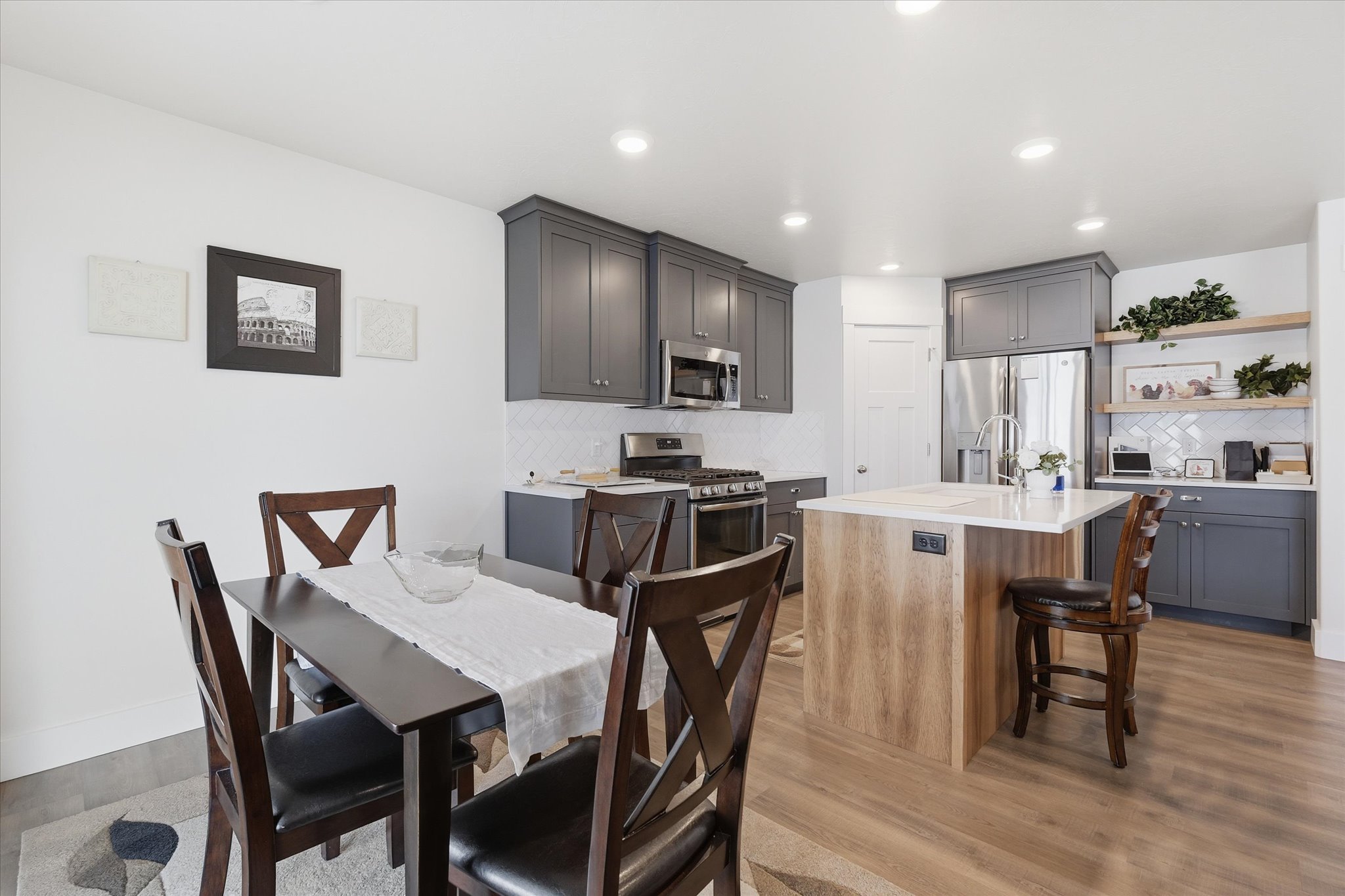 Spacious kitchen featuring gray shaker-style cabinetry, white backsplash tile, stainless steel appliances, a center island with wood-finish paneling and a light-toned countertop, and wood-finish flooring