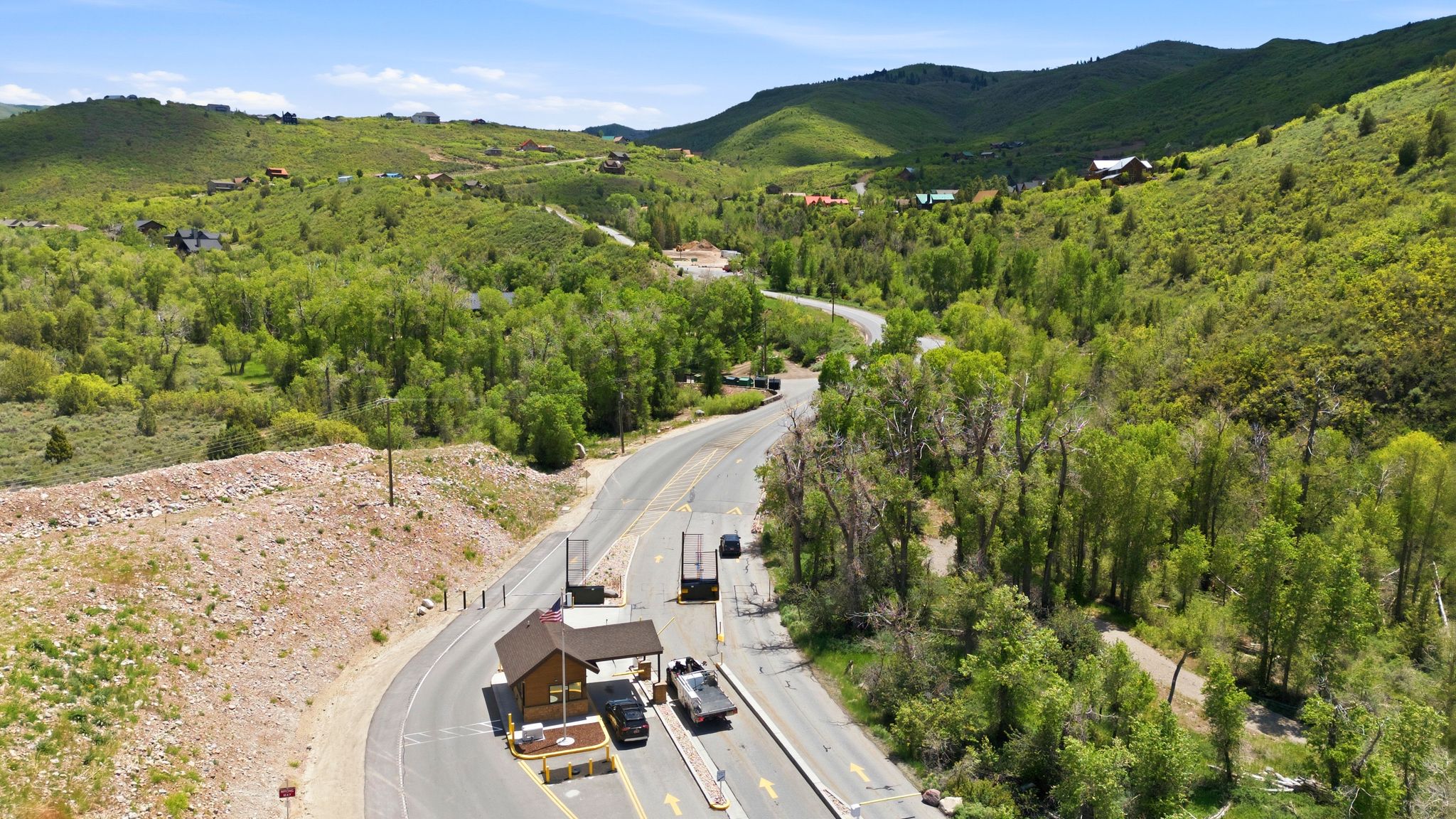 Roadway with a small entry station, surrounded by lush green hillsides and scattered residential properties
