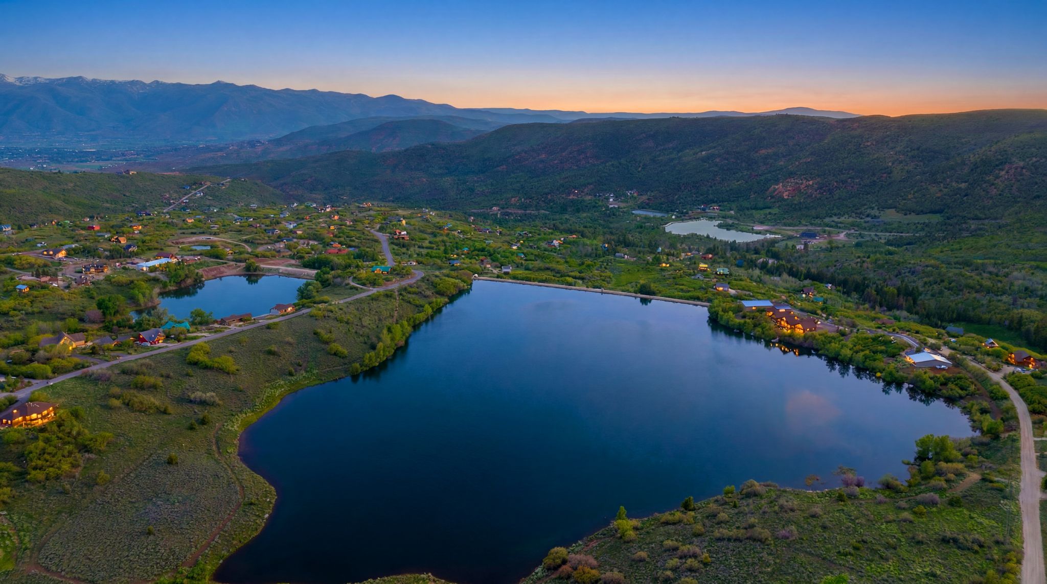 Expansive lakefront setting featuring multiple bodies of water surrounded by mountainous terrain and scattered residences