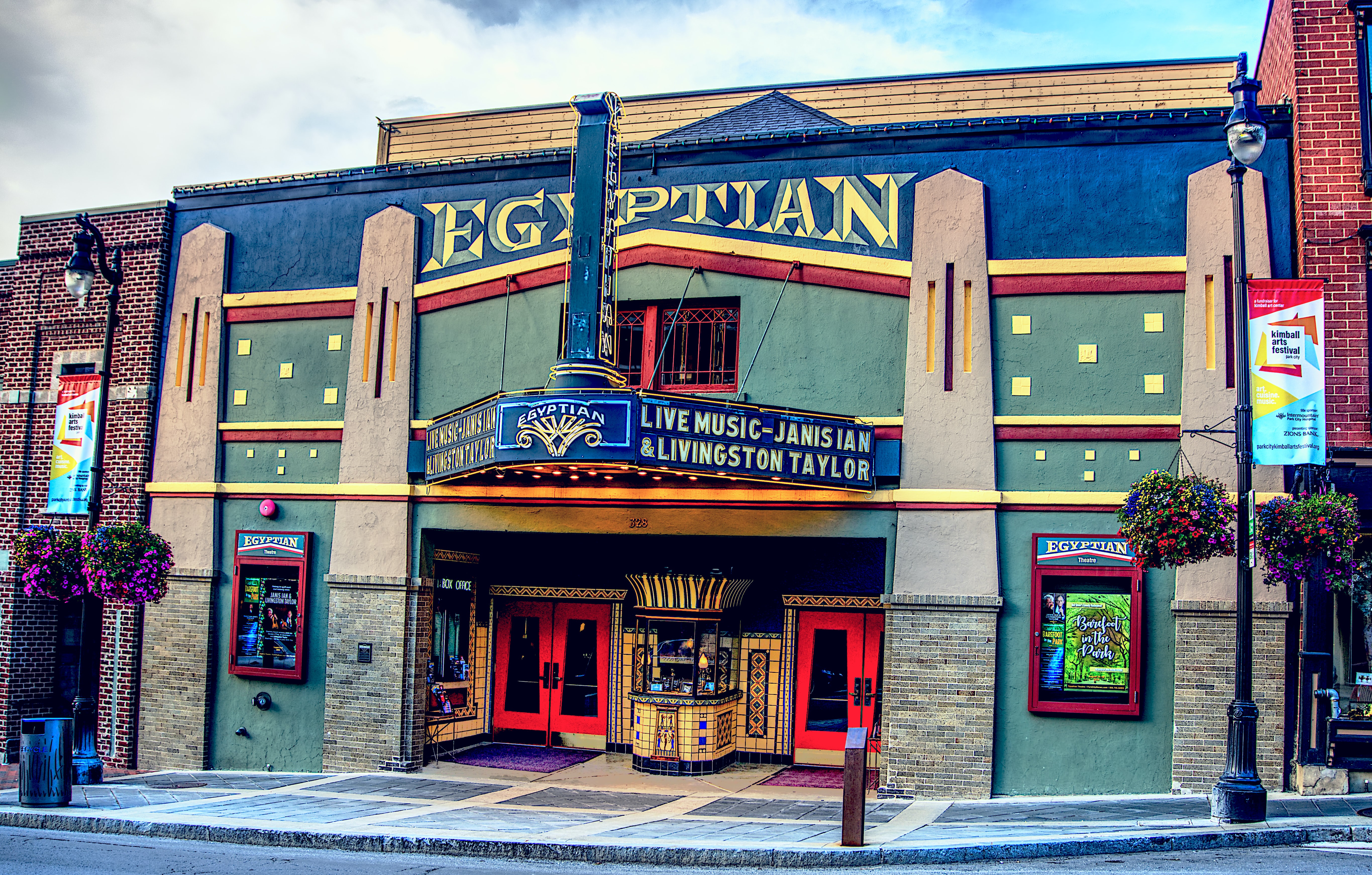 Art Deco style facade featuring a prominent marquee sign, red double entry doors, brick accents, and a sidewalk entrance