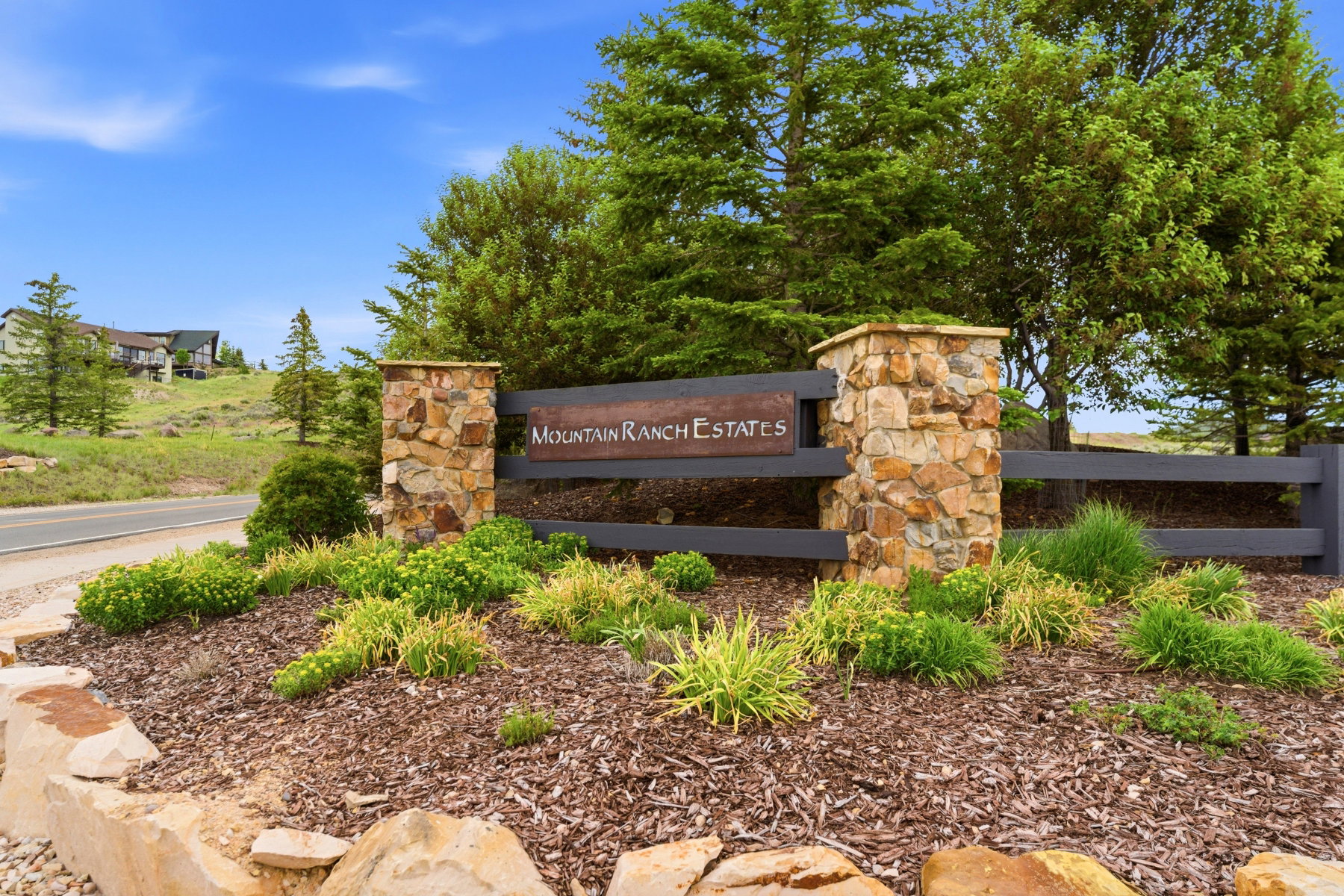 Stone and wood-finish entry sign for Mountain Ranch Estates, featuring decorative landscaping with various plantings and wood mulch