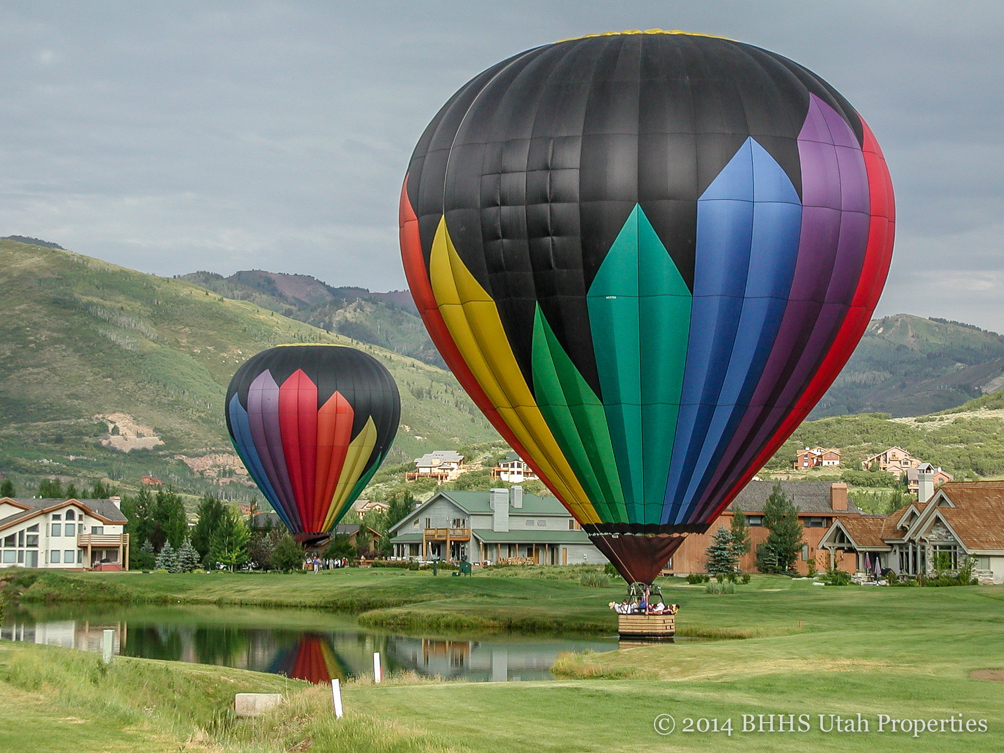 Promotional Image. Displaying residential structures and a body of water with two hot air balloons in the foreground