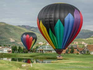 Promotional Image. Displaying residential structures and a body of water with two hot air balloons in the foreground