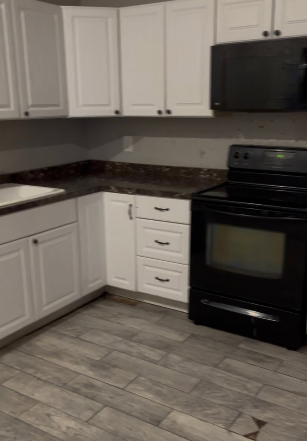 Kitchen featuring white upper and lower cabinetry, dark countertops, a black range, and a black microwave