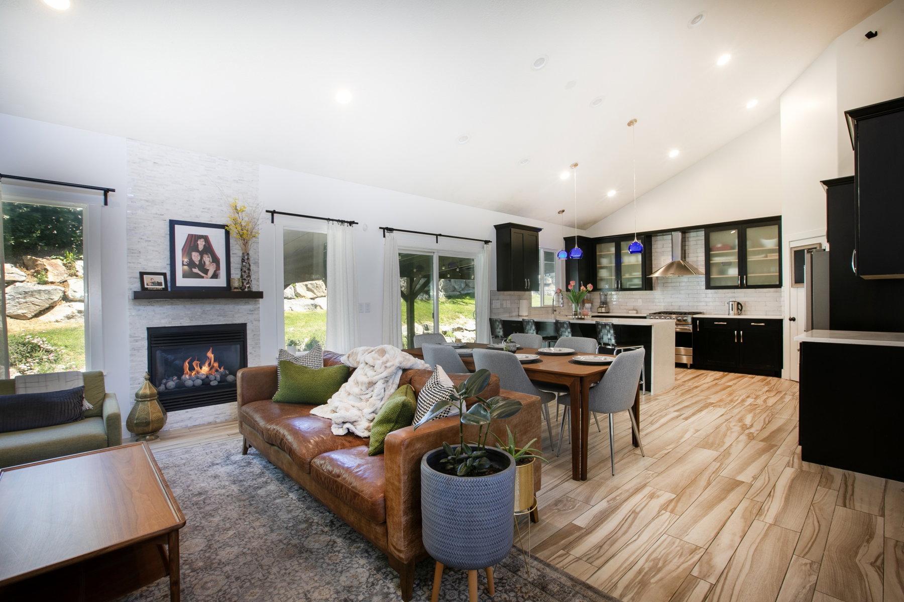 Vaulted ceiling living space featuring a tiled fireplace with dark wood mantel, wood-finish flooring, recessed lighting, and sliding glass doors to the exterior