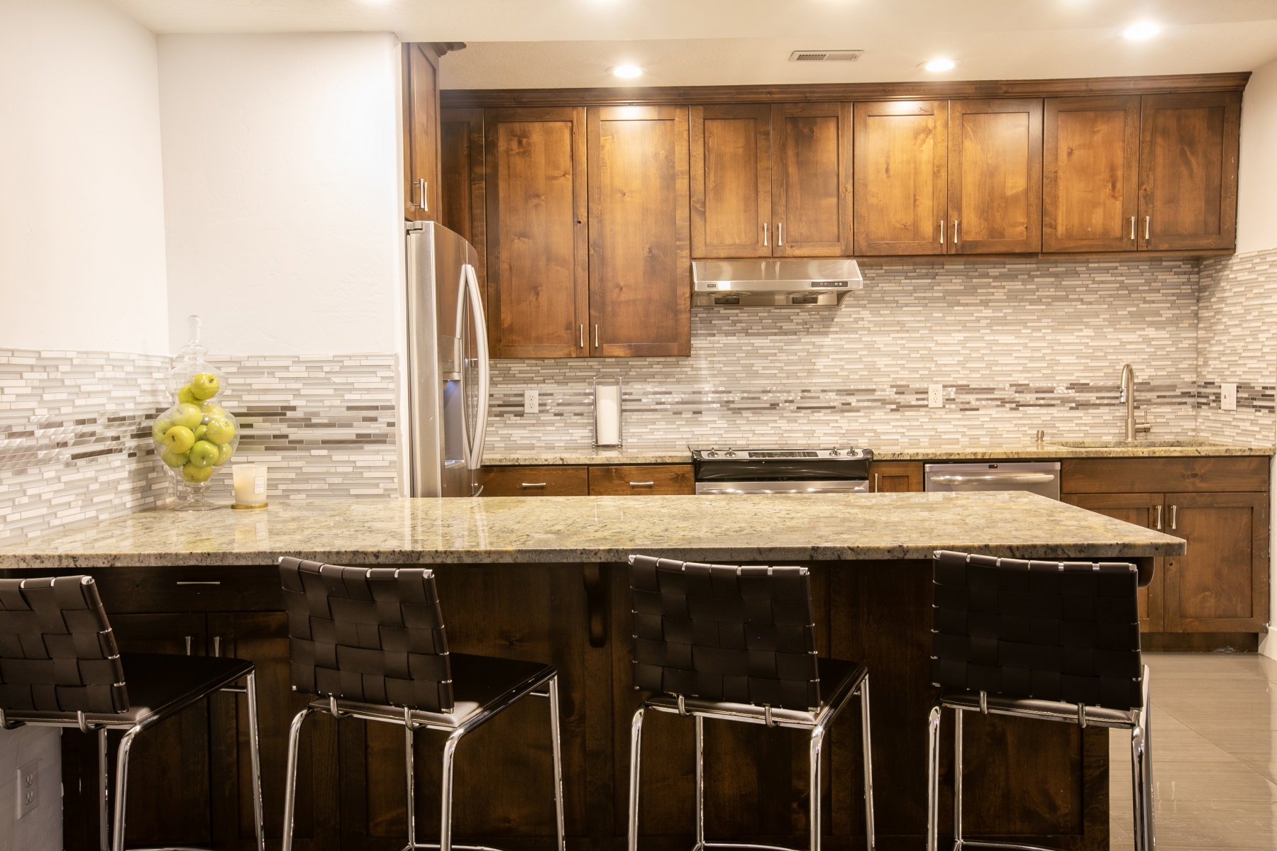 Kitchen featuring an island with stone countertop, stainless steel appliances, wood cabinetry, and a mosaic tile backsplash